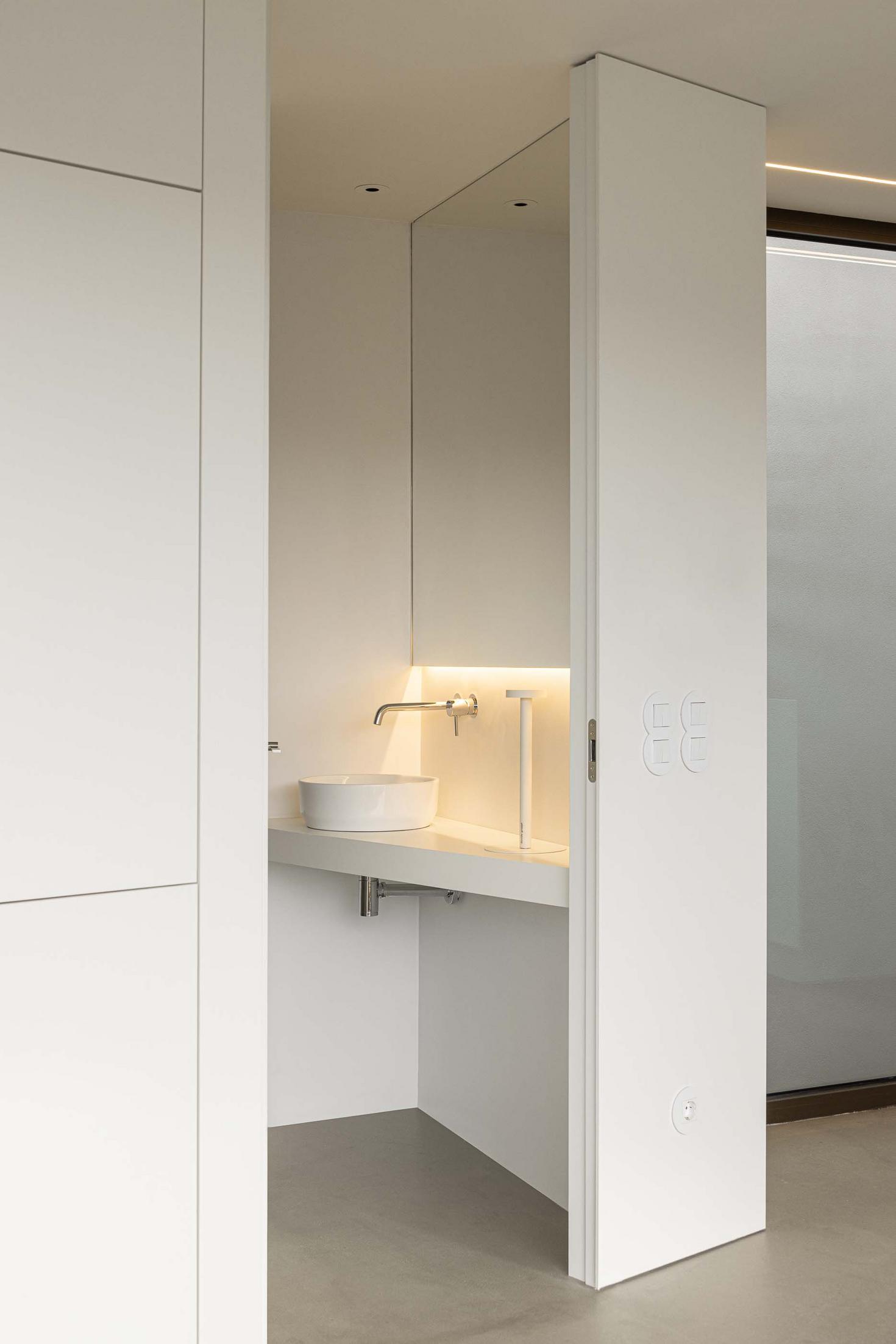 Casa de banho minimalista com lavatório de pousar branco sobre bancada. Espelho e paredes brancas, iluminação LED integrada — Beira Mar II arquitectura Paulo Martins fotografia Ivo Tavares