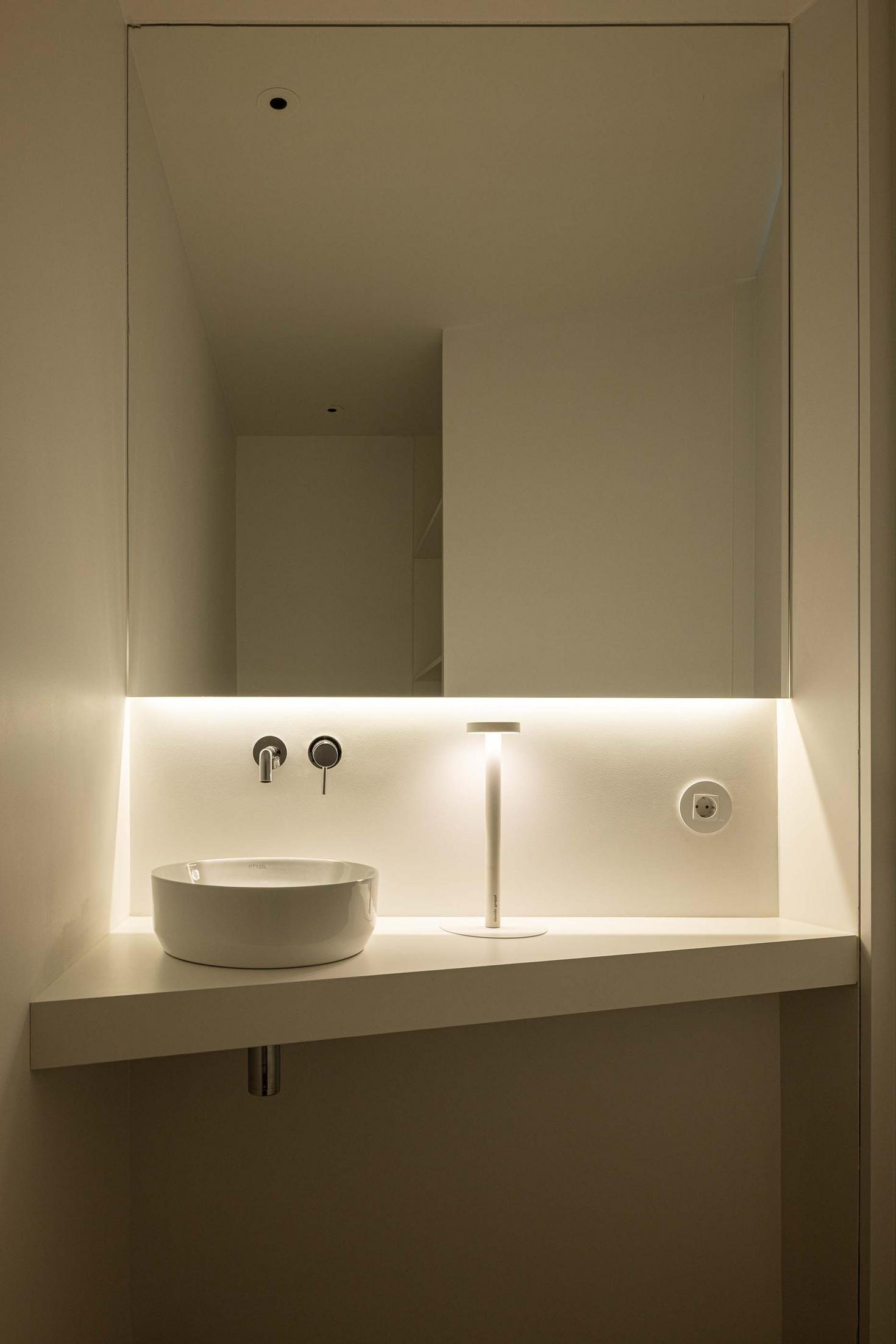 Lavatório de pousar branco sobre bancada, com espelho grande e iluminação LED. Torneira de parede cromada e candeeiro de mesa — Beira Mar II arquitectura Paulo Martins fotografia Ivo Tavares