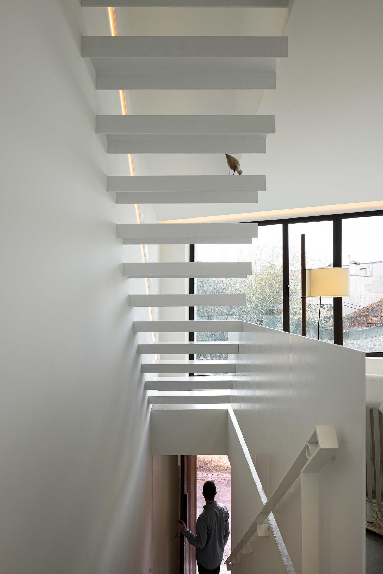 Escada flutuante branca, com degraus em consola, ligando pavimentos. Iluminação linear embutida na parede. Vão envidraçado lateral — Beira Mar II arquitectura Paulo Martins fotografia Ivo Tavares