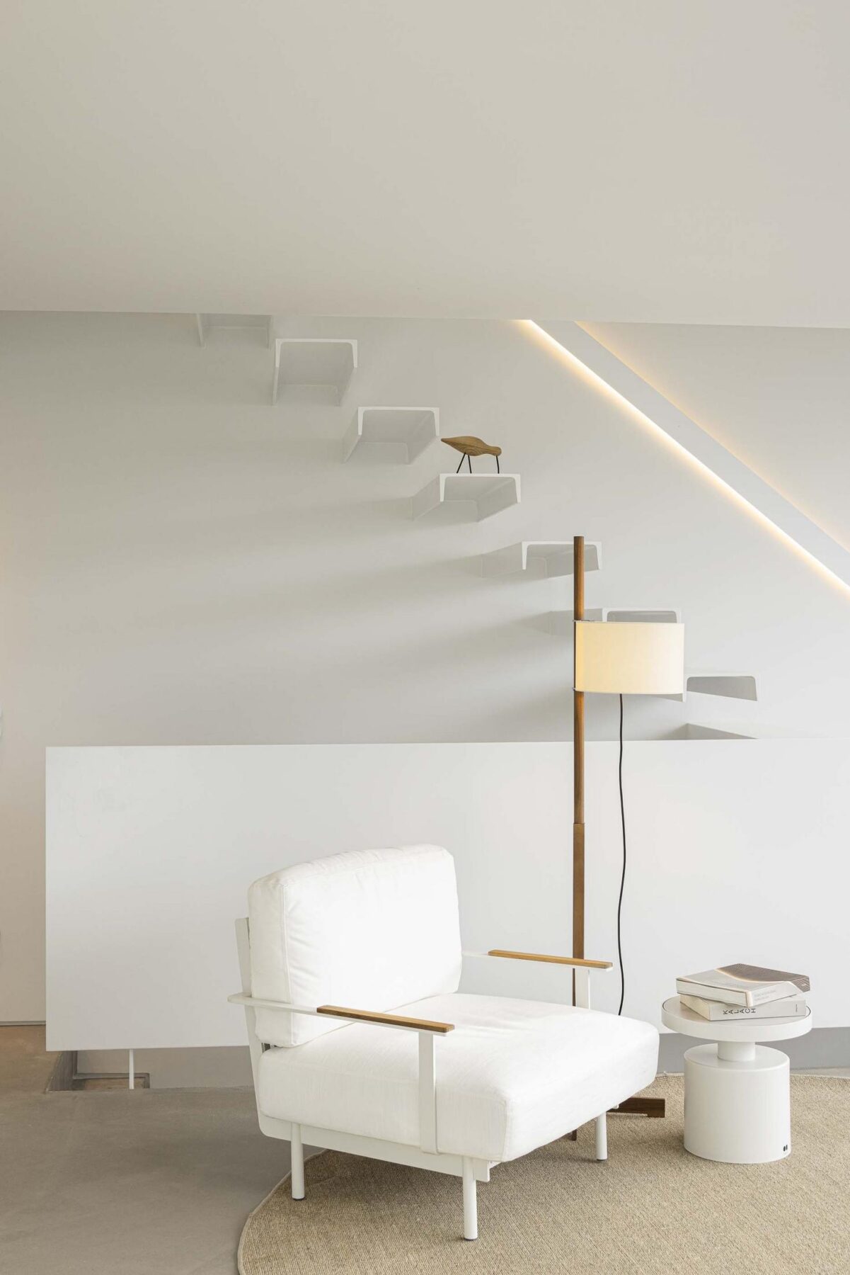 Sala de estar: Sala de estar minimalista com poltrona branca, candeeiro de pé e escadas flutuantes. — Beira Mar II arquitetura Paulo Martins Arquitectura e Design em Aveiro