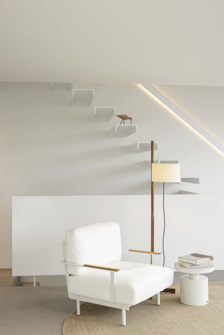 Sala de estar: Sala de estar minimalista com poltrona branca, candeeiro de pé e escadas flutuantes. — Beira Mar II arquitetura Paulo Martins Arquitectura e Design em Aveiro