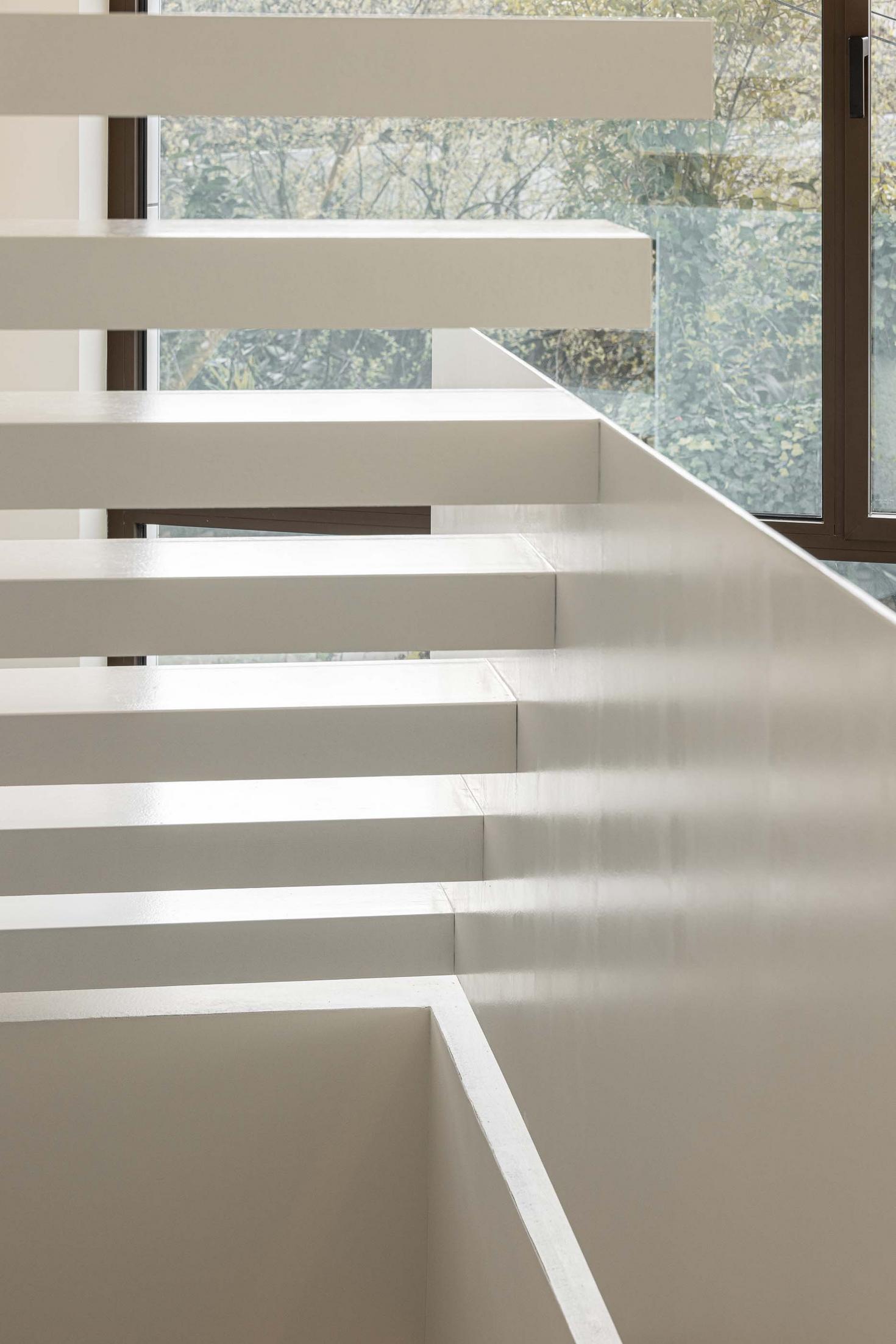 Detalhe da escada flutuante branca, com degraus em consola. Guarda-corpos em vidro transparente. Vista para vegetação exterior — Beira Mar II arquitectura Paulo Martins fotografia Ivo Tavares