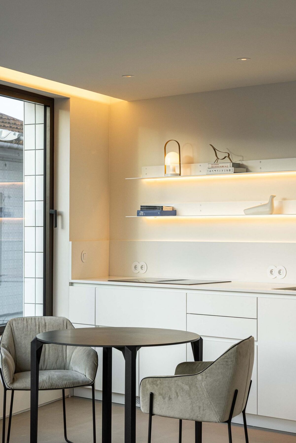 Cozinha: Detalhe da cozinha branca com mesa de jantar, cadeiras e prateleiras iluminadas. — Beira Mar II arquitetura Paulo Martins Arquitectura e Design em Aveiro