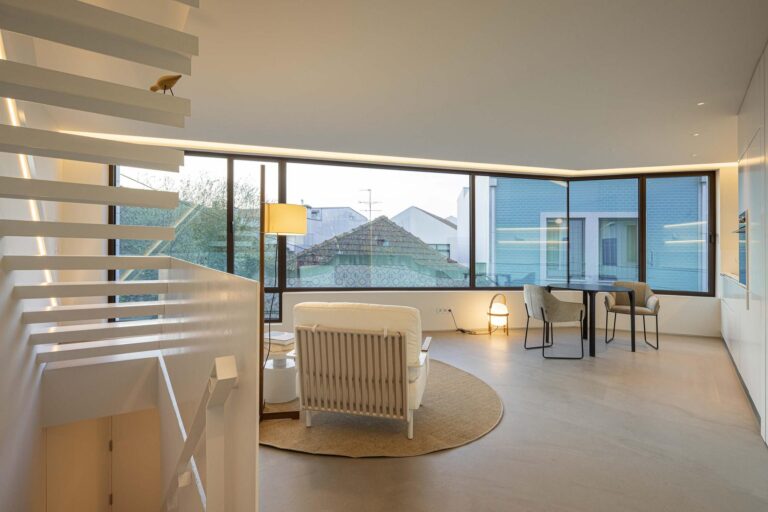 Sala de estar: Vista ampla da sala de estar com cozinha integrada, escadas flutuantes e grande janela. — Beira Mar II arquitetura Paulo Martins Arquitectura e Design em Aveiro