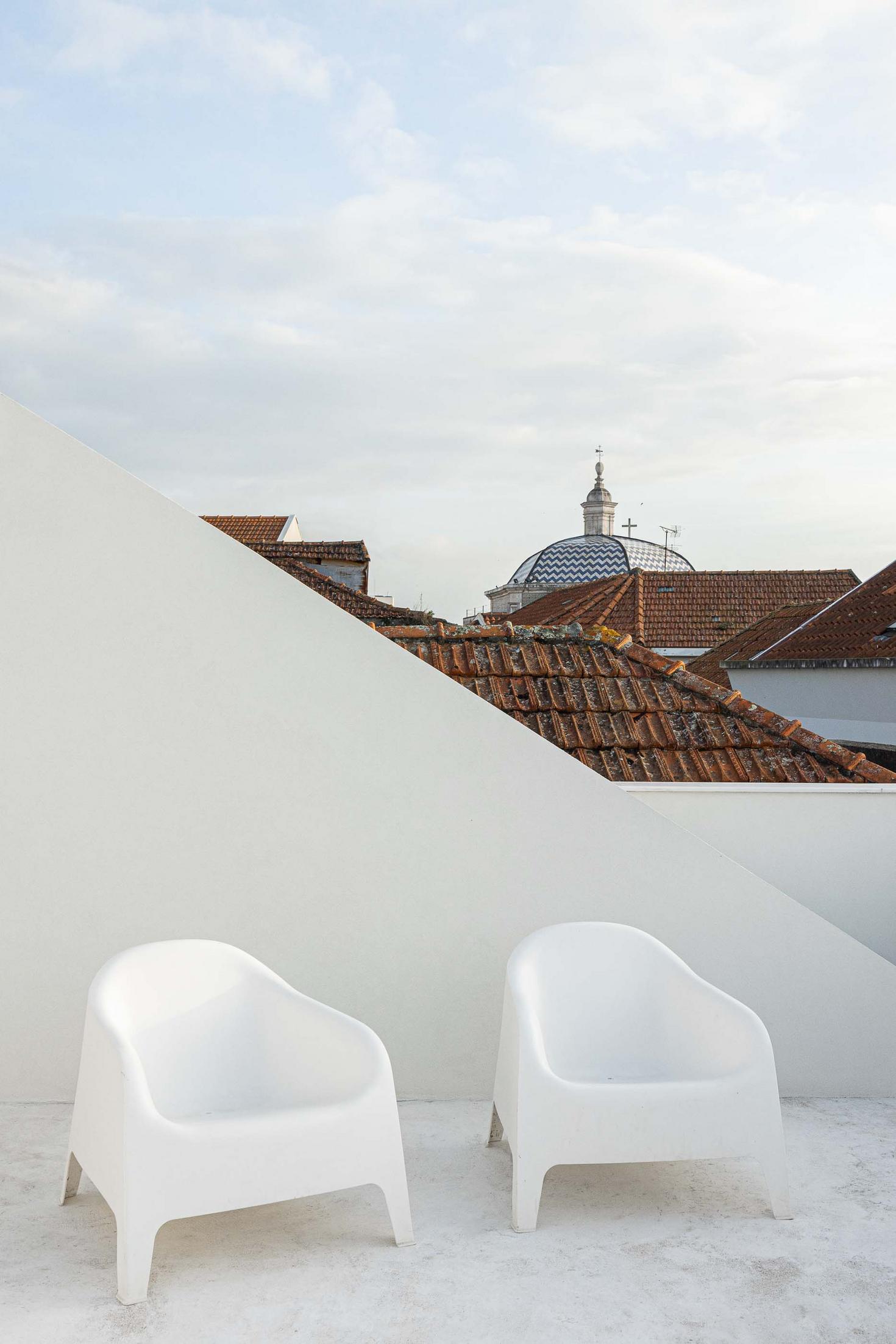 Terraço da cobertura com duas cadeiras brancas. Vista para telhados de barro e a cúpula de São Gonçalinho. Paredes brancas angulares — Beira Mar II arquitectura Paulo Martins fotografia Ivo Tavares