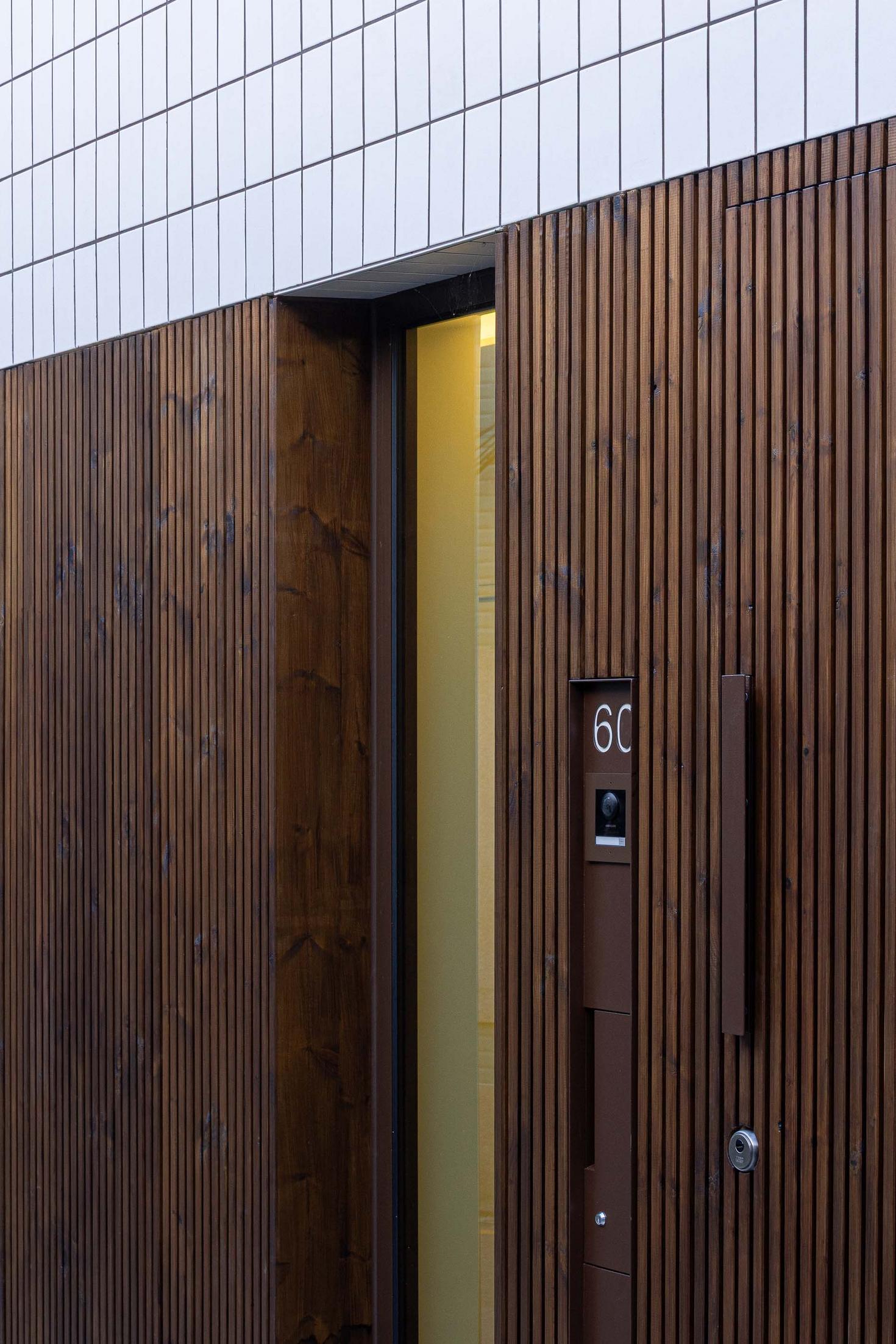 Detalhe da entrada com porta em ripado de madeira escura. Intercomunicador e puxador em metal oxidado. Fachada superior em azulejo branco — Beira Mar II arquitectura Paulo Martins fotografia Ivo Tavares
