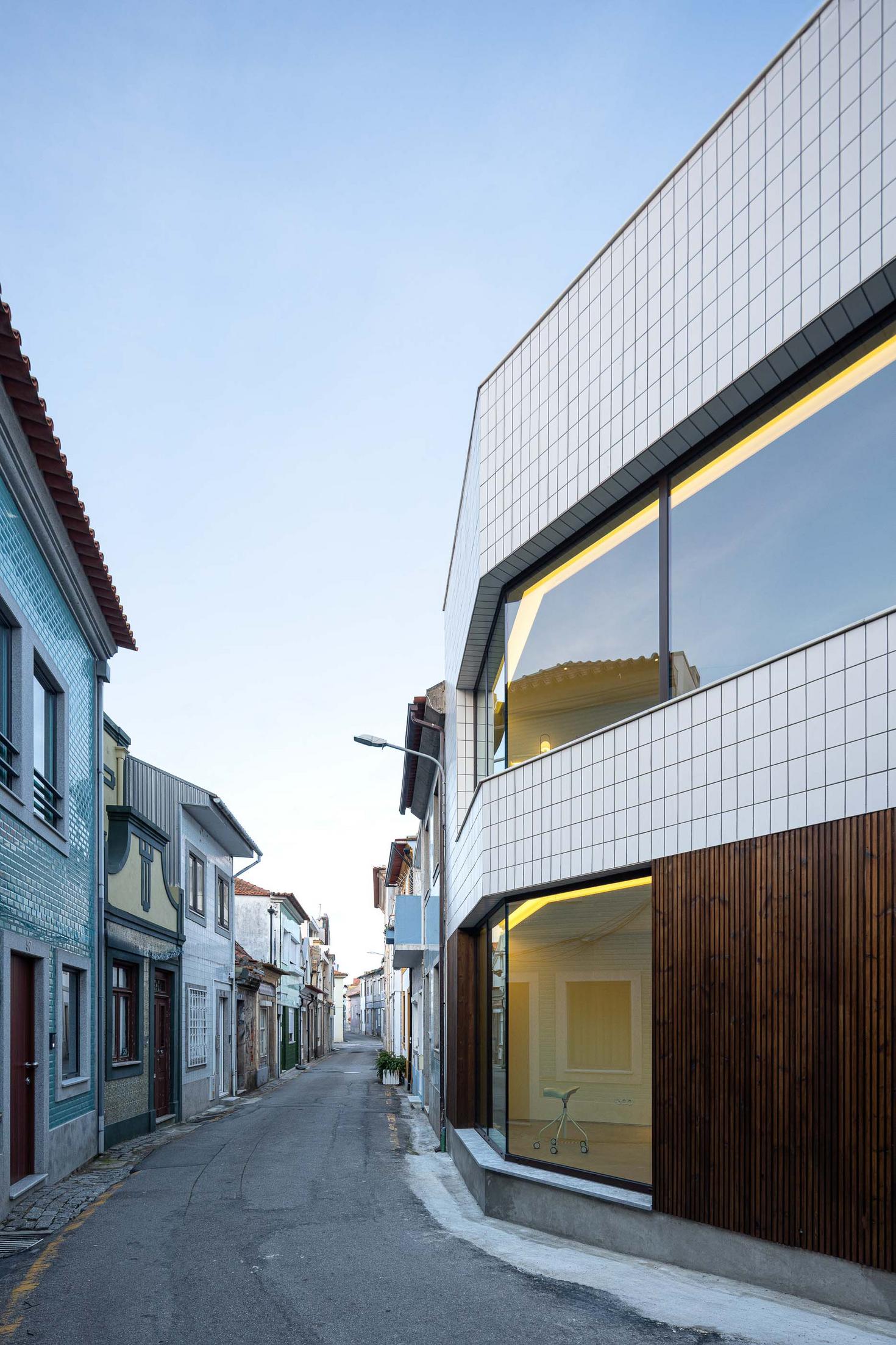 Fachada da moradia com ripado de madeira e azulejo branco, integrada na rua estreita. Vãos envidraçados refletem o contexto urbano — Beira Mar II arquitectura Paulo Martins fotografia Ivo Tavares
