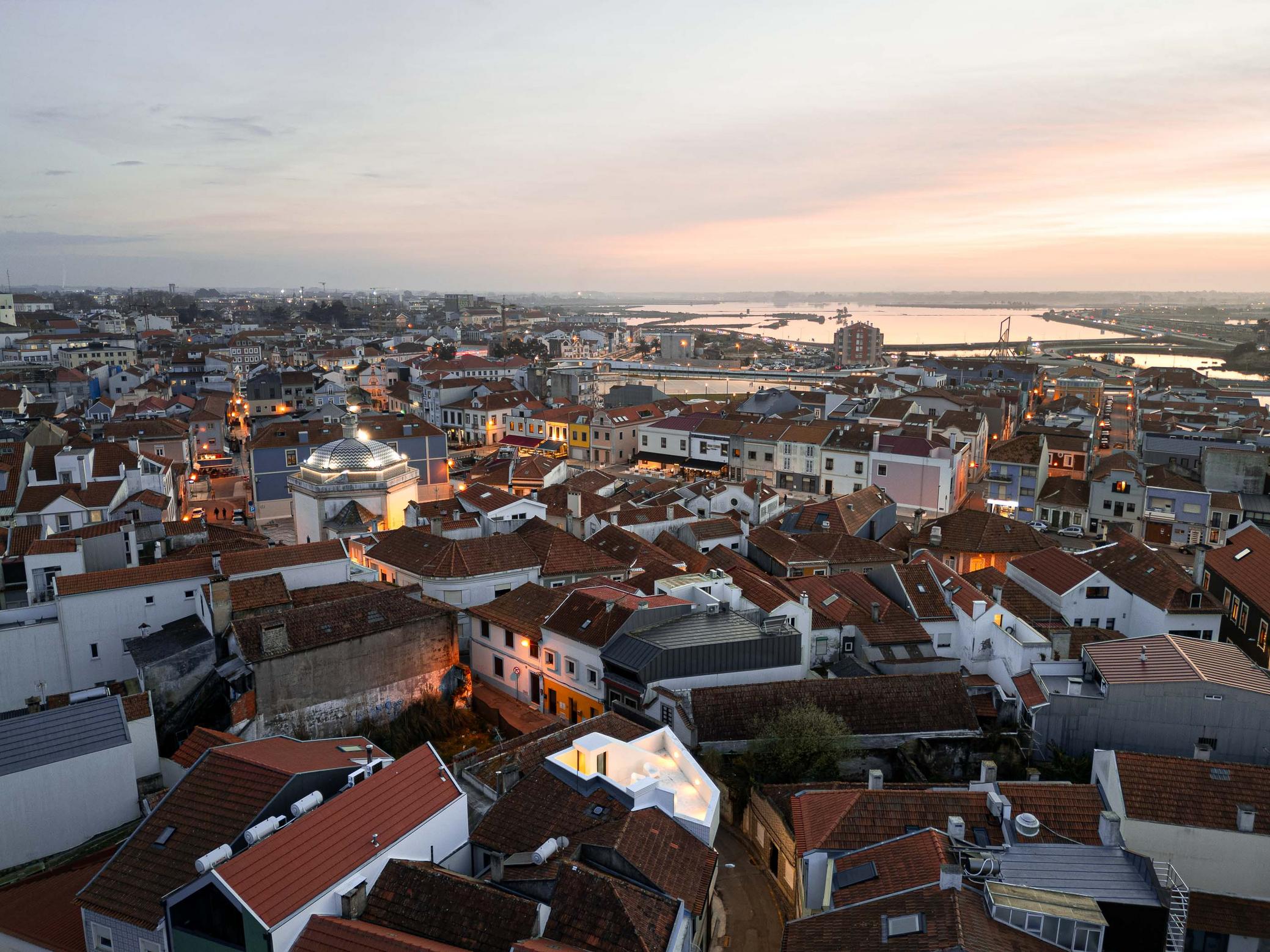 Cobertura da moradia branca, com telhados de barro circundantes e cúpula de São Gonçalinho. Céu alaranjado ao fundo — Beira Mar II arquitectura Paulo Martins fotografia Ivo Tavares