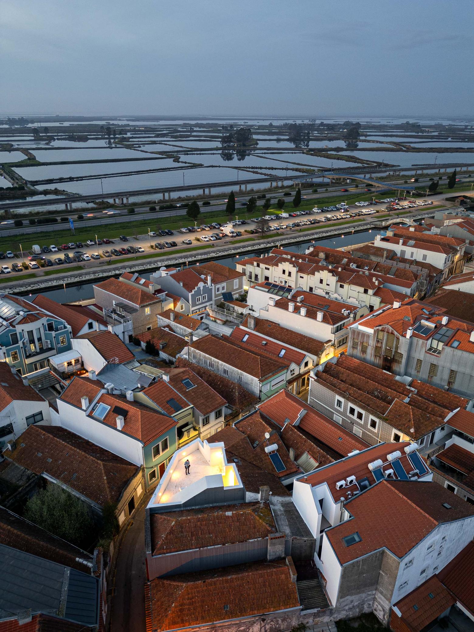 Cobertura da moradia branca, com pessoa, inserida em malha urbana de telhados de barro. Vistas para salinas e autoestrada — Beira Mar II arquitectura Paulo Martins fotografia Ivo Tavares