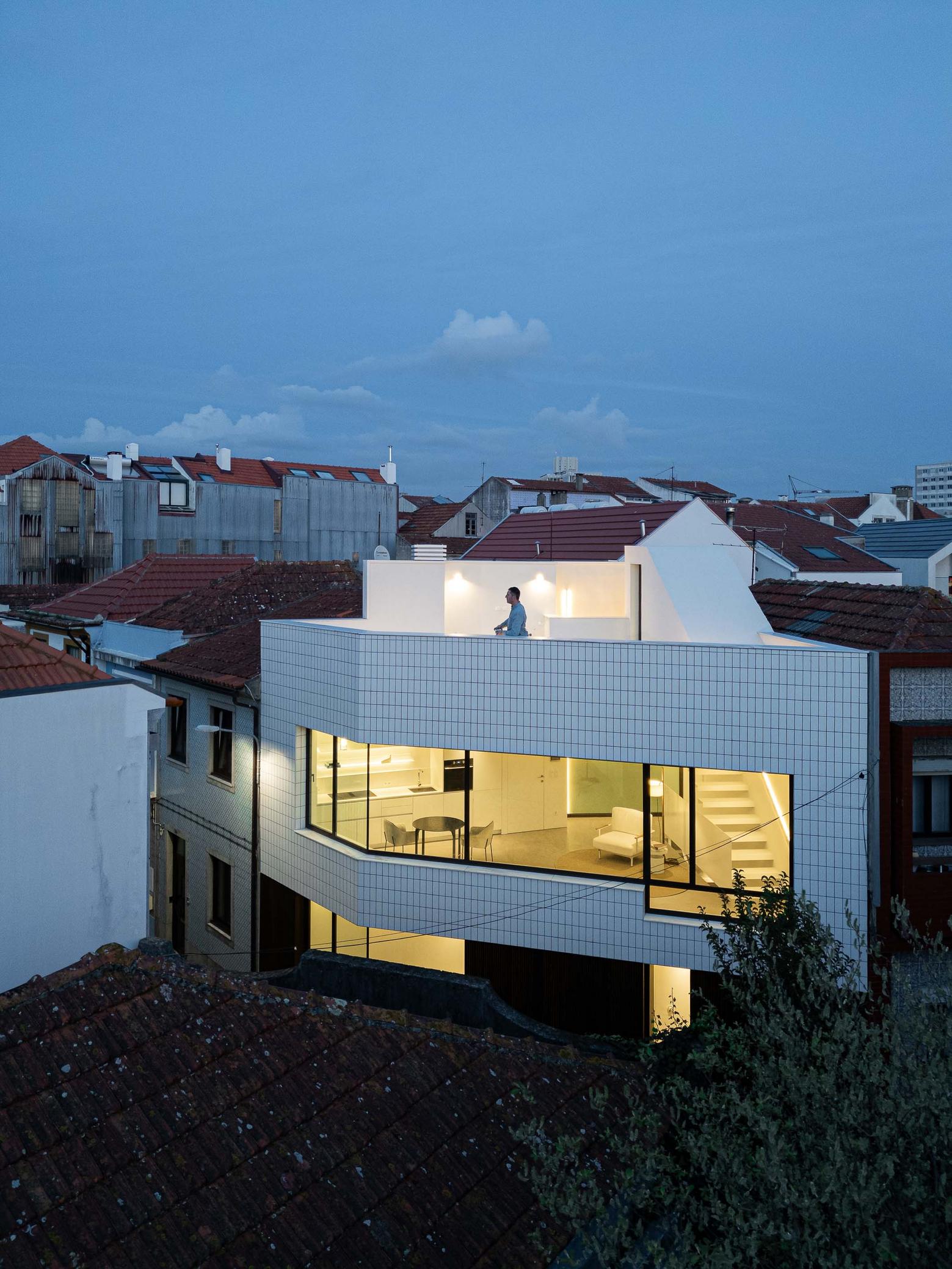Fachada da moradia com azulejo branco e grande vão envidraçado. Terraço superior com paredes brancas e pessoa — Beira Mar II arquitectura Paulo Martins fotografia Ivo Tavares