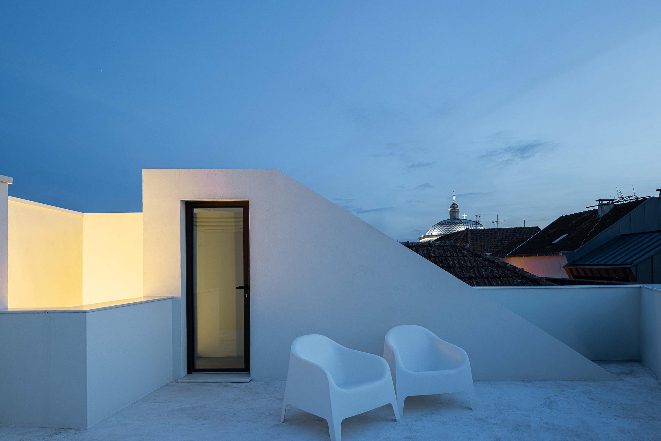 Terraço da cobertura com paredes brancas angulares e iluminação embutida. Porta de acesso envidraçada. Duas cadeiras brancas — Beira Mar II arquitectura Paulo Martins fotografia Ivo Tavares