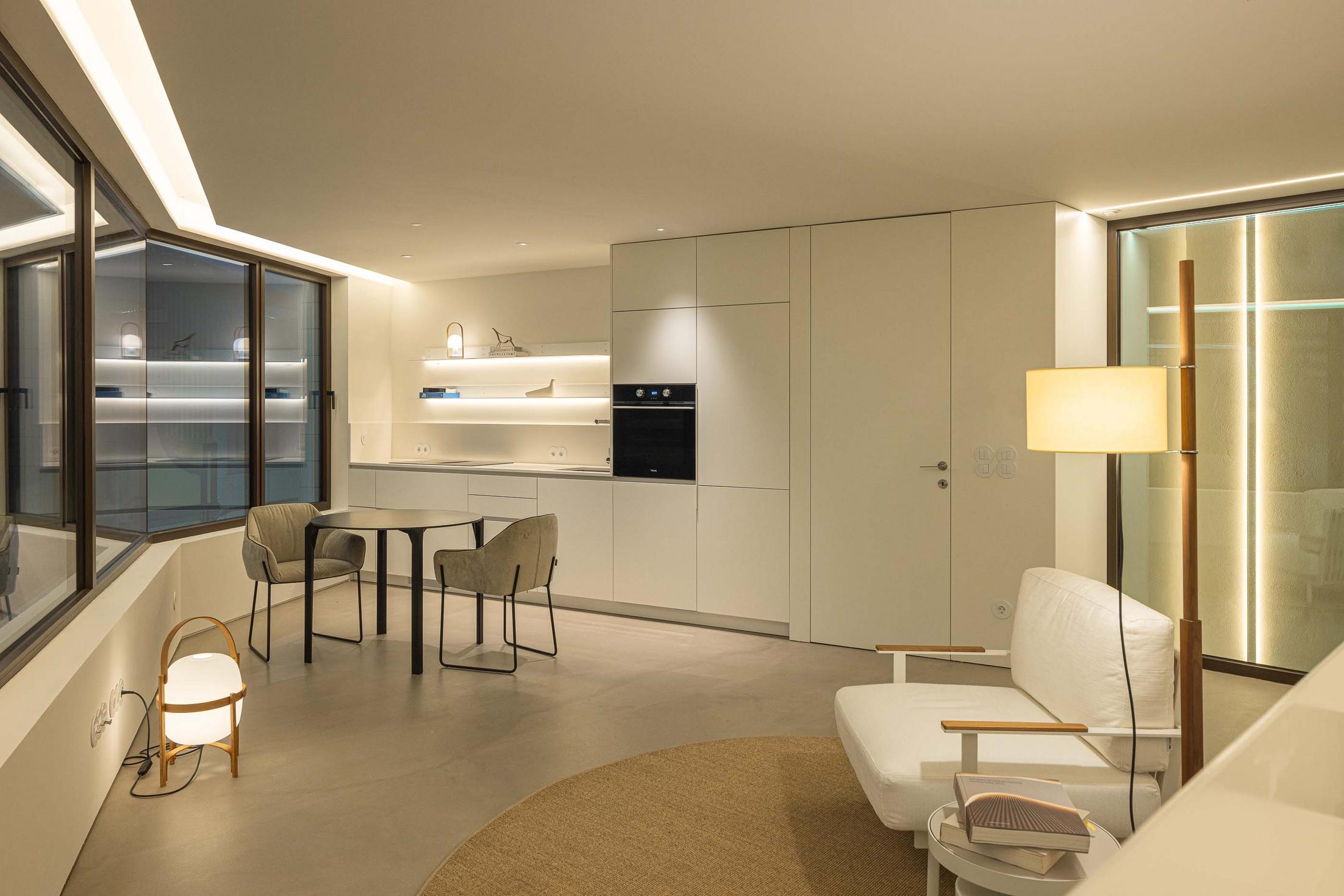 Espaço social em planta aberta com sala e cozinha. Iluminação LED embutida e candeeiro de pé. Grande vão envidraçado — Beira Mar II arquitectura Paulo Martins fotografia Ivo Tavares