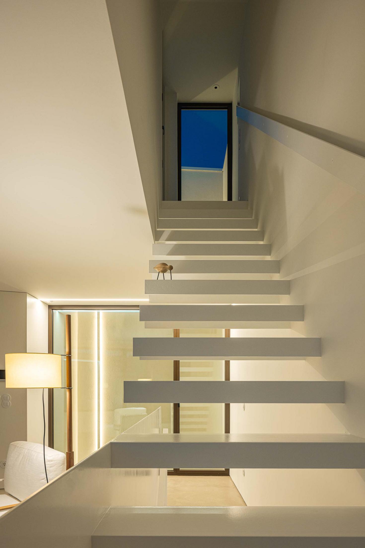 Escada flutuante branca, com degraus em consola, ligando pavimentos. Iluminação linear embutida. Porta de acesso ao terraço visível — Beira Mar II arquitectura Paulo Martins fotografia Ivo Tavares