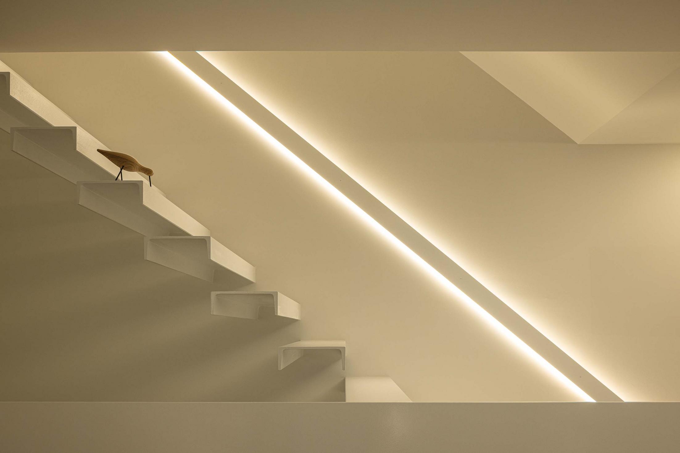 Detalhe da escada flutuante branca com iluminação linear embutida na parede. Escultura de pássaro em madeira — Beira Mar II arquitectura Paulo Martins fotografia Ivo Tavares