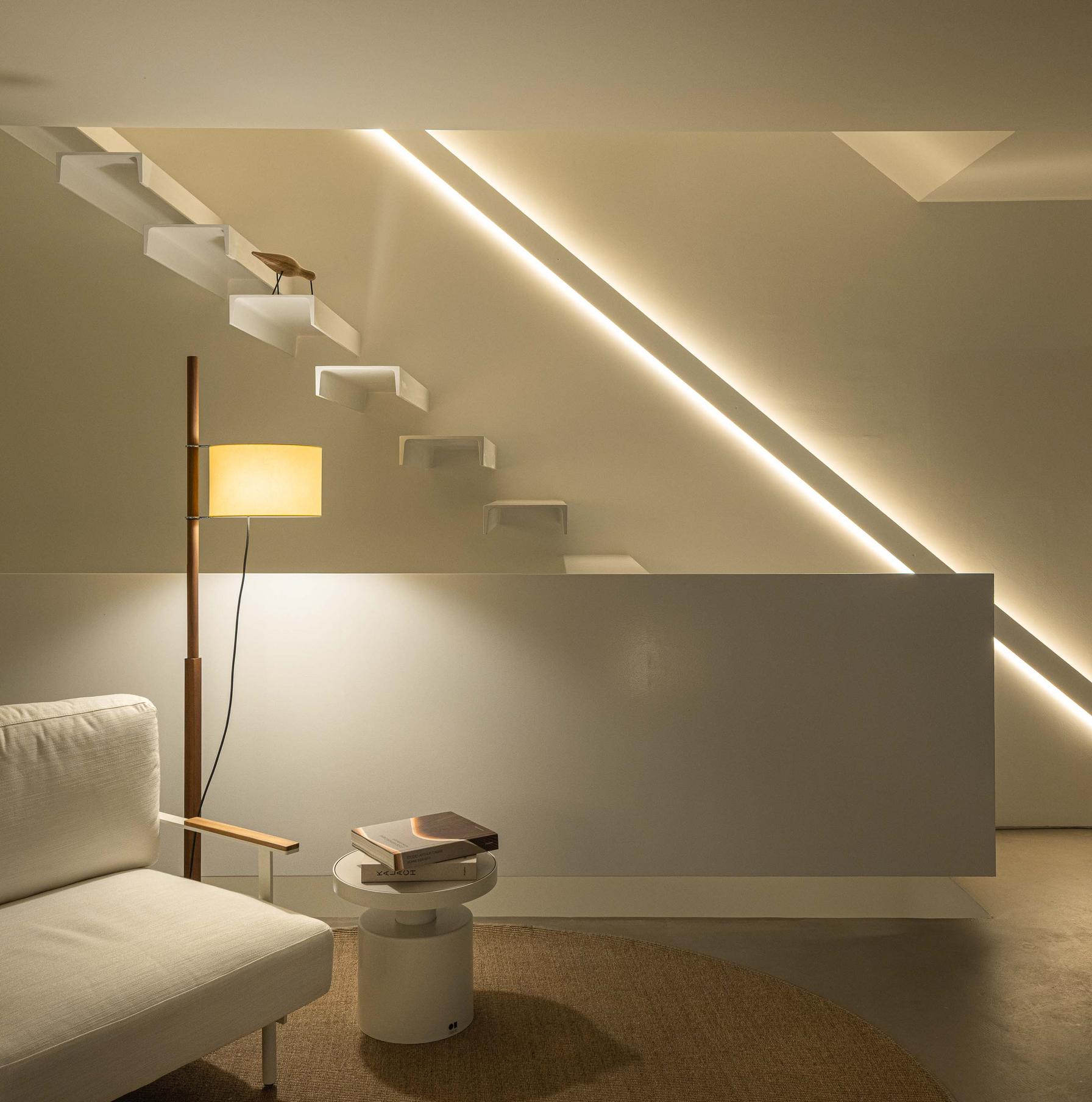 Sala com poltrona branca e candeeiro de pé. Escada flutuante branca e iluminação linear embutida na parede. Pavimento em cimento afagado — Beira Mar II arquitectura Paulo Martins fotografia Ivo Tavares