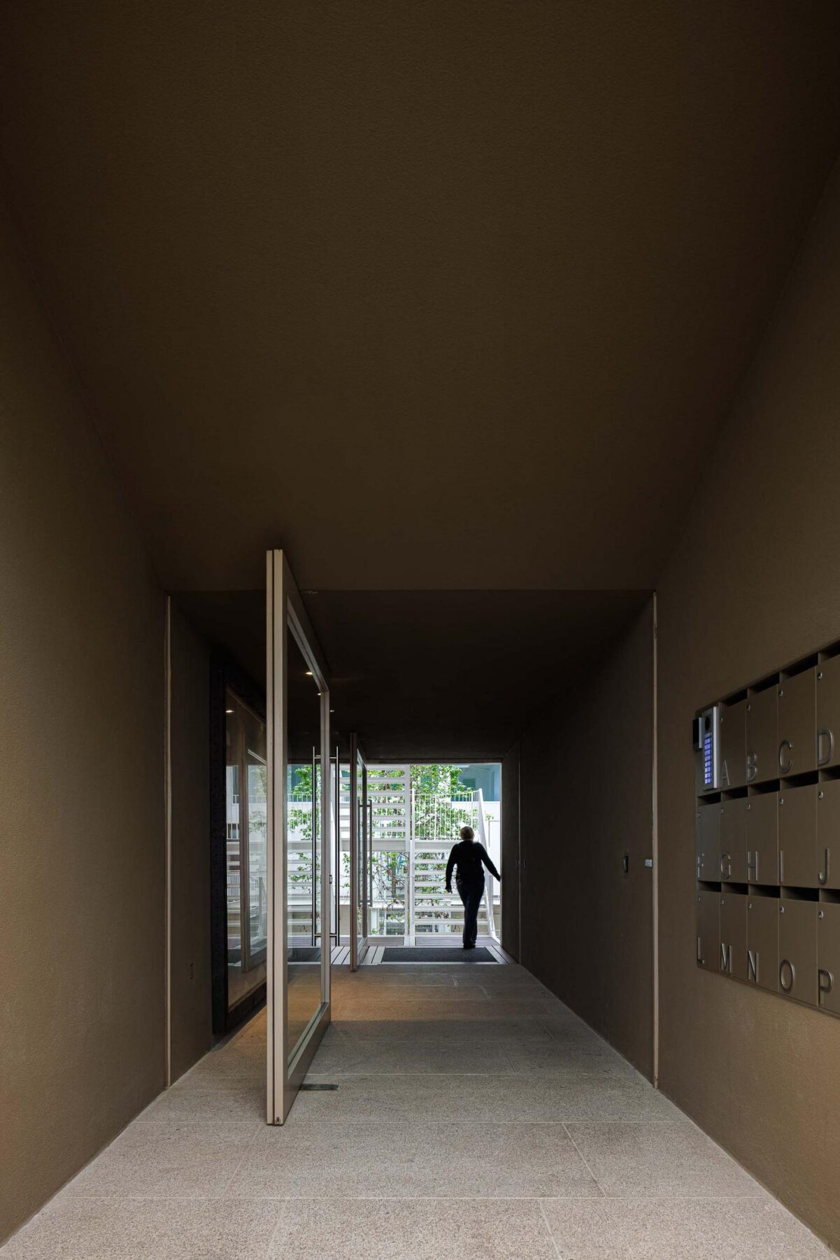 Corredor: Longo corredor com pavimento em pedra, paredes castanhas e caixas de correio metálicas. — Assembleia da Granja arquitetura Lousinha Arquitectos em Vila Nova de Gaia