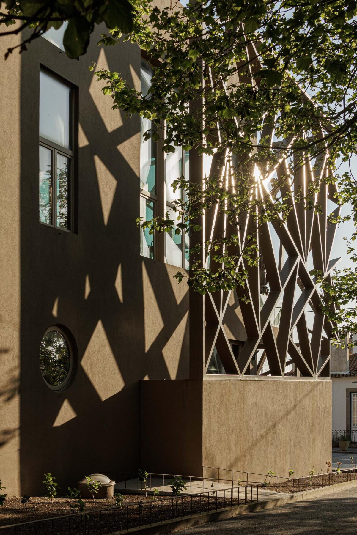 Exterior: Fachada com estrutura metálica, janela circular e vegetação. — Assembleia da Granja arquitetura Lousinha Arquitectos em Vila Nova de Gaia