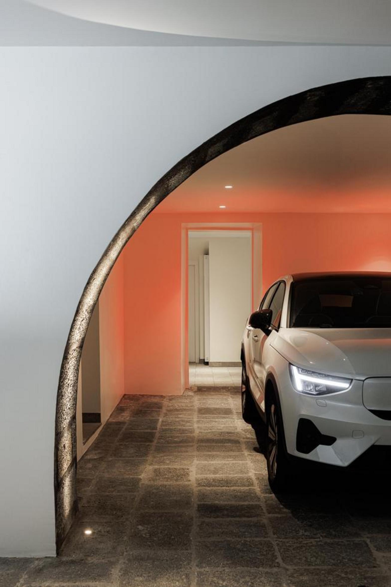 Garagem. Pavimento em pedra cinzenta. Arco de pedra rústica iluminado. Carro branco estacionado, paredes brancas — Casa T+A Açores arquitectura Lopes da Costa fotografia Ivo Tavares
