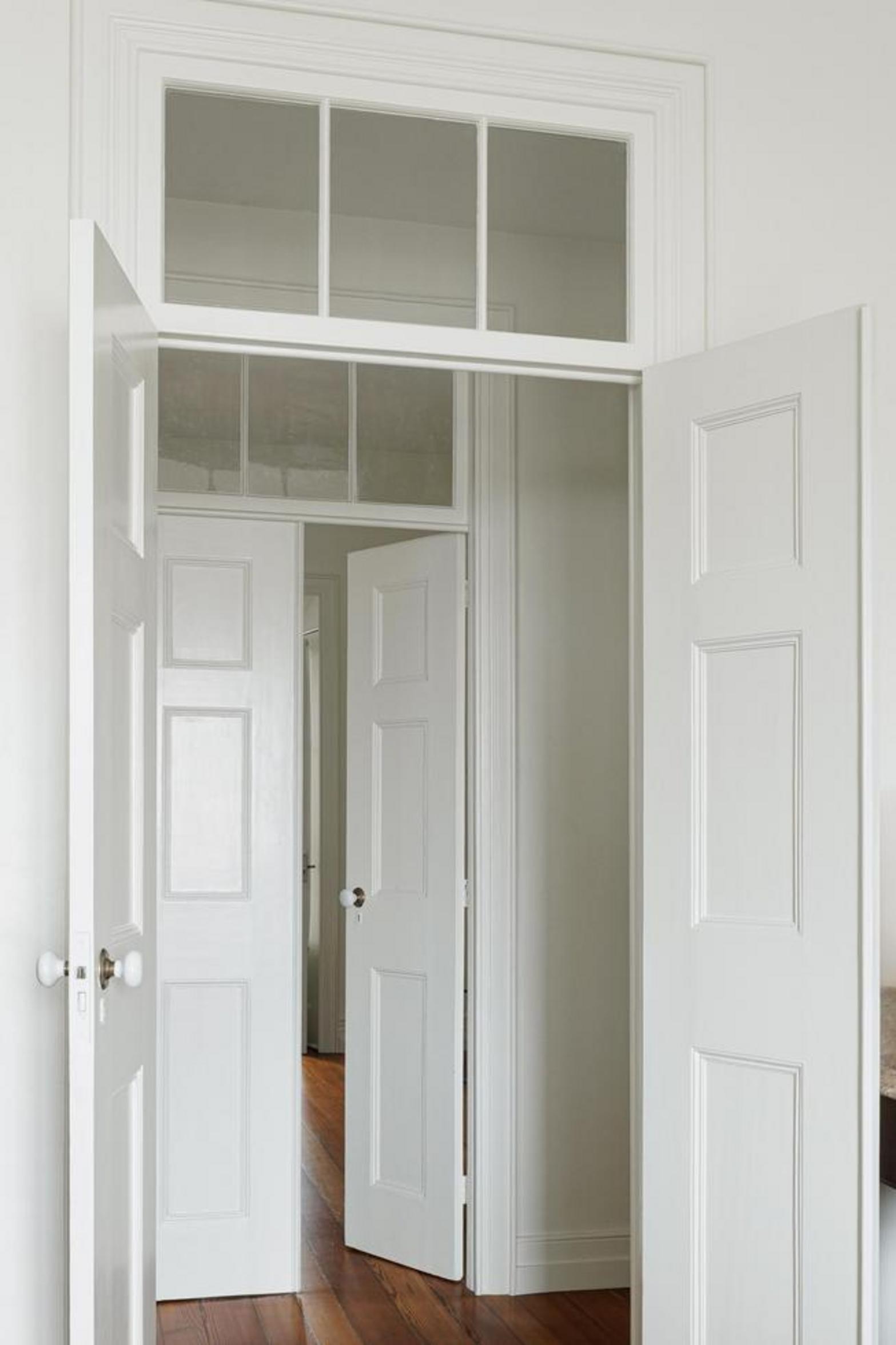 Corredor. Pavimento em madeira mel, paredes brancas. Vãos de porta em arco. Luz natural e focos no pavimento — Casa T+A Açores arquitectura Lopes da Costa fotografia Ivo Tavares