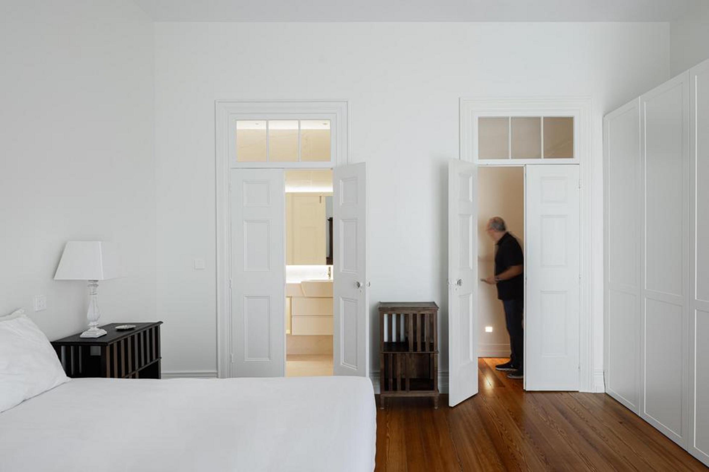 Quarto/Escritório. Pavimento em madeira mel. Armários brancos embutidos com secretária de madeira. Vista para casa de banho — Casa T+A Açores arquitectura Lopes da Costa fotografia Ivo Tavares
