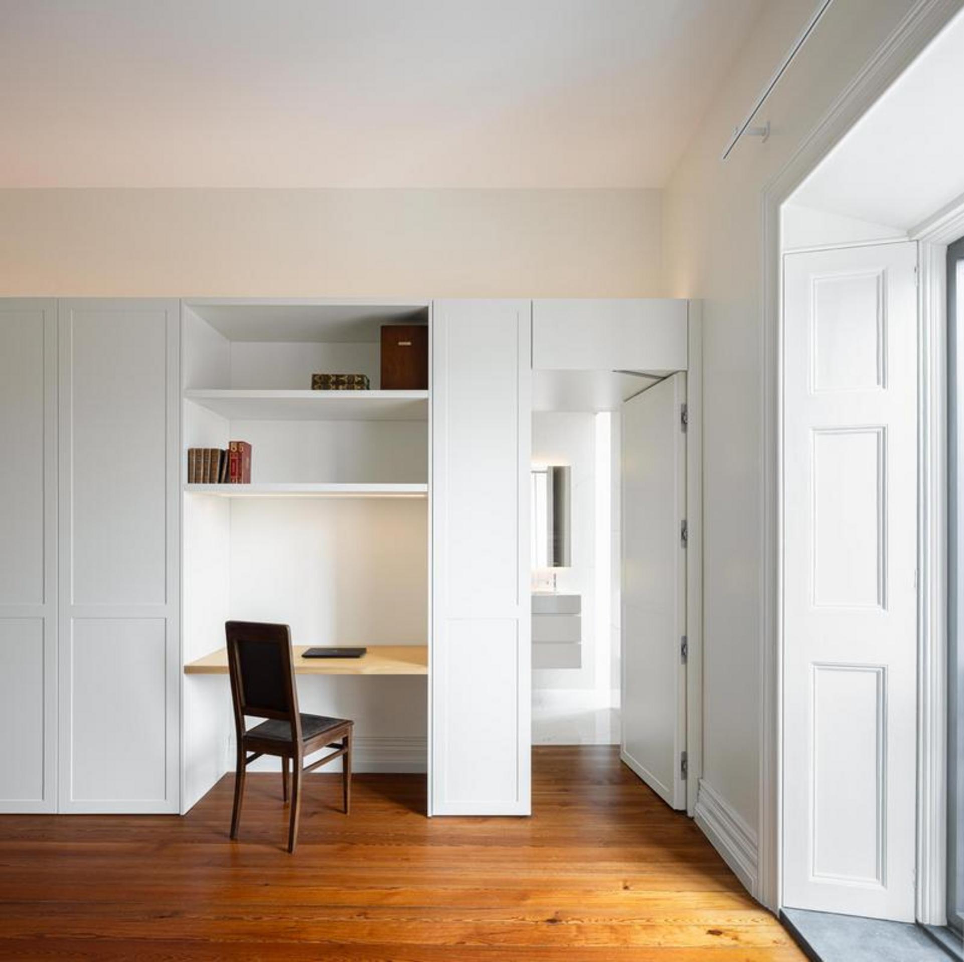 Corredor/Casa de banho. Corredor estreito branco com pavimento em madeira escura. Vista para casa de banho branca com mármore — Casa T+A Açores arquitectura Lopes da Costa fotografia Ivo Tavares