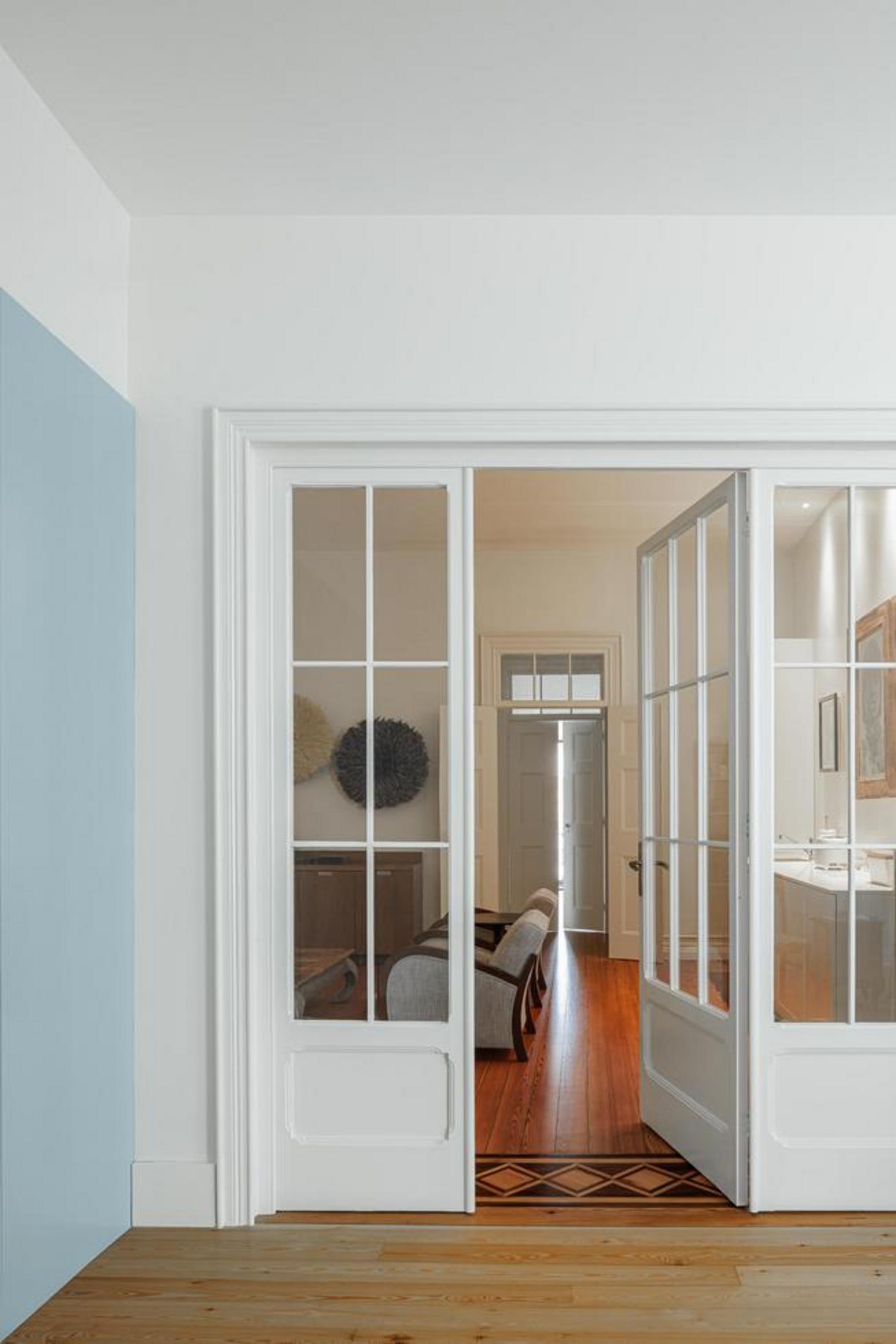 Casa de banho. Vista através de porta azul clara. Pavimento e paredes em mármore branco, móvel suspenso branco com nicho iluminado — Casa T+A Açores arquitectura Lopes da Costa fotografia Ivo Tavares