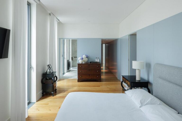 Quarto com pavimento em madeira e paredes brancas, beneficiando de ampla luz natural através de um vão de janela tradicional, ambiente sereno. — Casa T+A Açores . T+A . Azores House arquitectura Atelier d’arquitectura Lopes da Costa fotografia Ivo Tavares