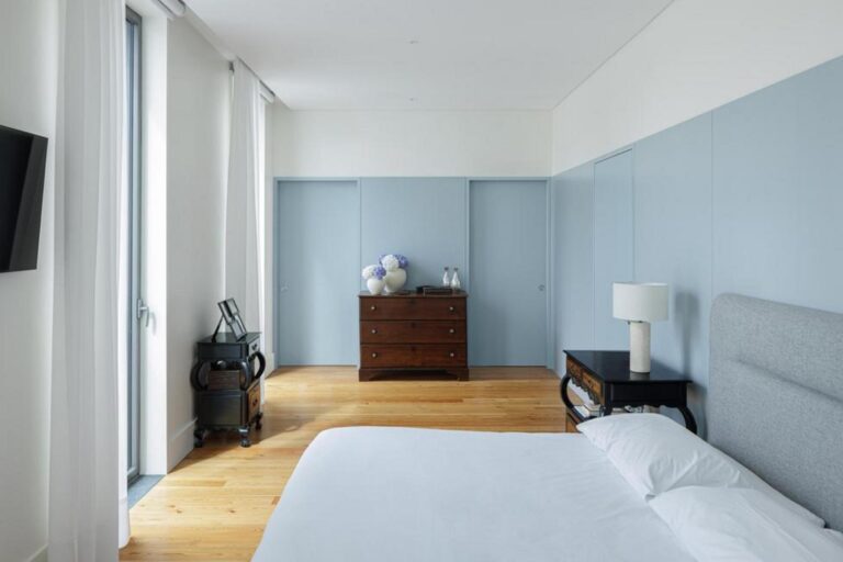 Casa de banho com revestimentos em pedra clara e lavatório suspenso, espelho grande e iluminação discreta, promovendo funcionalidade e conforto. — Casa T+A Açores . T+A . Azores House arquitectura Atelier d’arquitectura Lopes da Costa fotografia Ivo Tavares