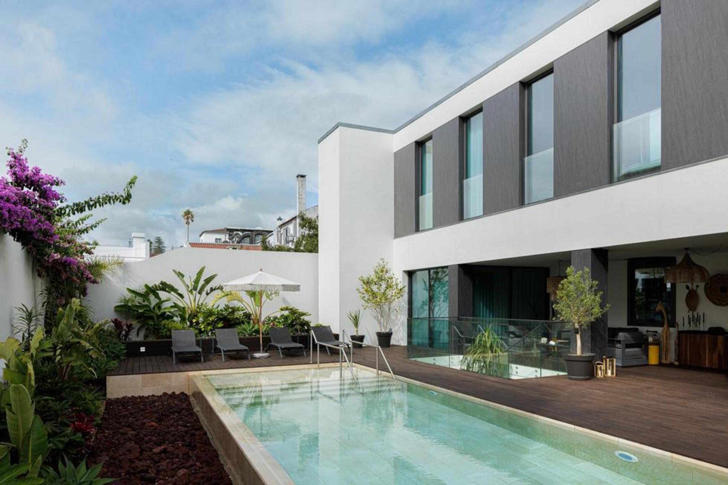 Jardim. Piscina retangular com borda de pedra clara. Parede branca com buganvília roxa, vegetação tropical verde — Casa T+A Açores arquitectura Lopes da Costa fotografia Ivo Tavares