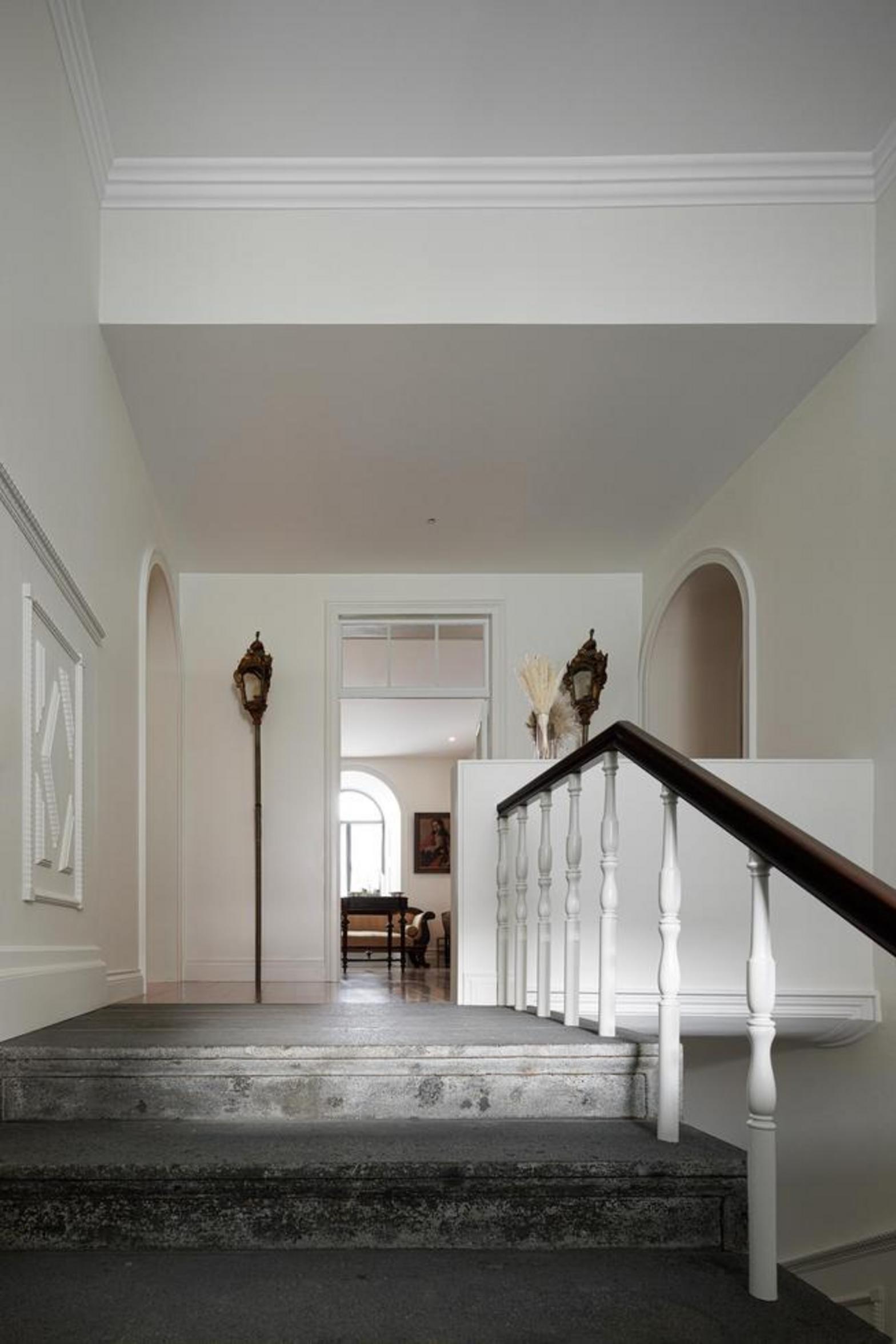 Escada. Degraus de madeira mel, corrimão preto. Arco branco. Espelho em arco no patamar superior — Casa T+A Açores arquitectura Lopes da Costa fotografia Ivo Tavares