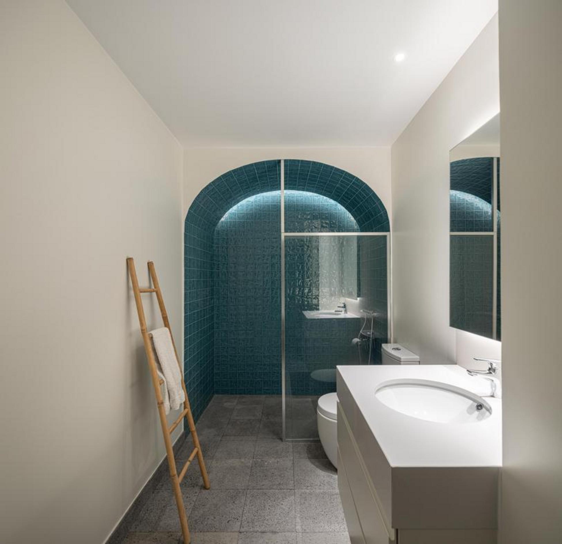 Entrada/Corredor. Pavimento em pedra cinzenta. Arcos de pedra rústica iluminados. Porta de vidro ao fundo — Casa T+A Açores arquitectura Lopes da Costa fotografia Ivo Tavares