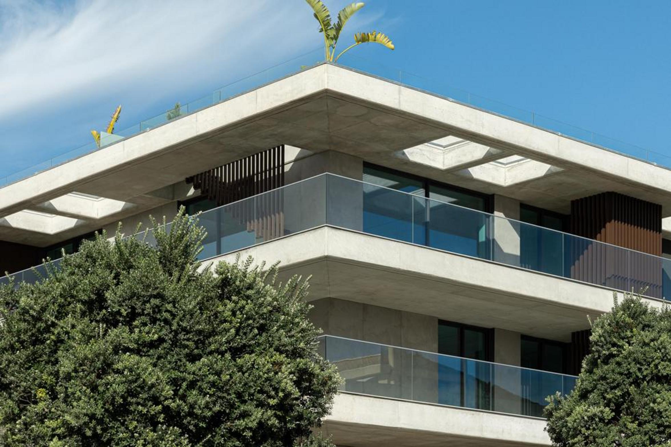 Canto do edifício com lajes de betão aparente em consola, guardas de vidro e vegetação na cobertura, sob céu azul — Edifício Scala-Mare arquitectura Lopes da Costa fotografia Ivo Tavares