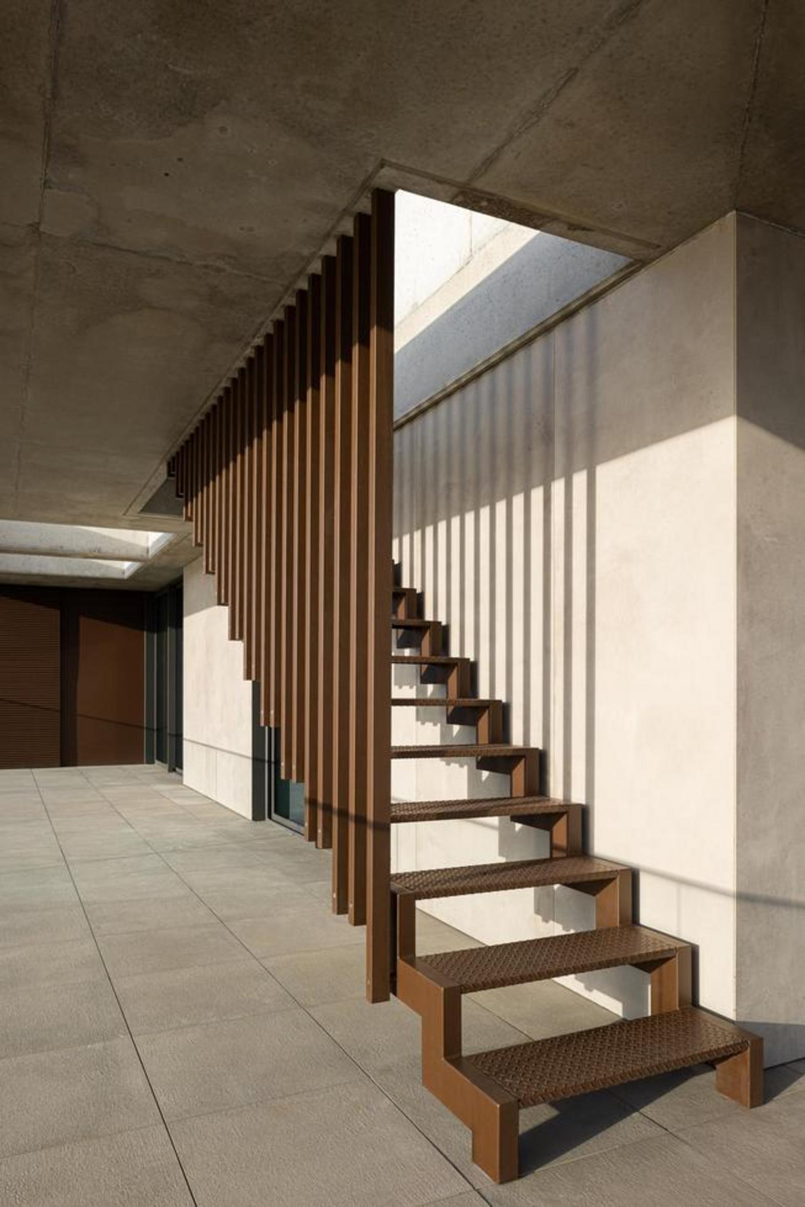 Escada exterior metálica em aço oxidado com degraus perfurados, sob uma laje de betão aparente, com luz e sombra — Edifício Scala-Mare arquitectura Lopes da Costa fotografia Ivo Tavares