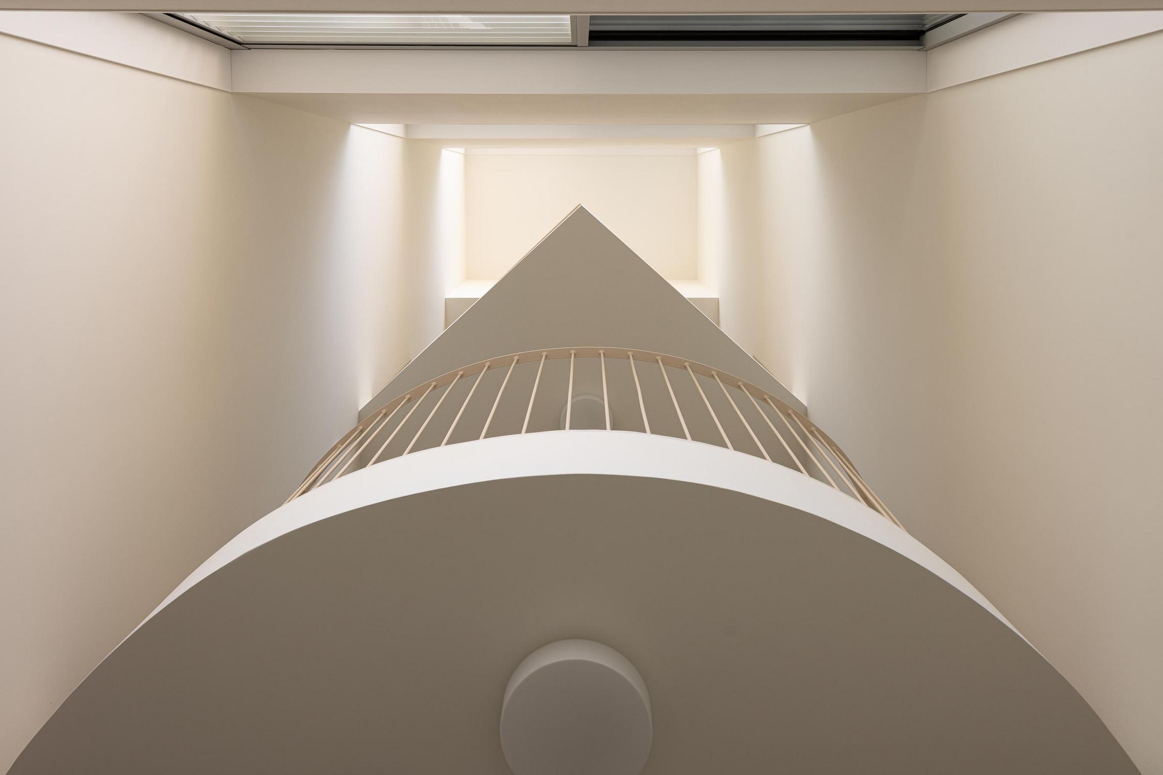 Vão de escada vertical com iluminação zenital. Guardas metálicas claras e paredes curvas em branco mate criam um efeito escultórico — Edifício Multifamiliar Hintze Ribeiro arquitectura Helder da Rocha fotografia Ivo Tavares