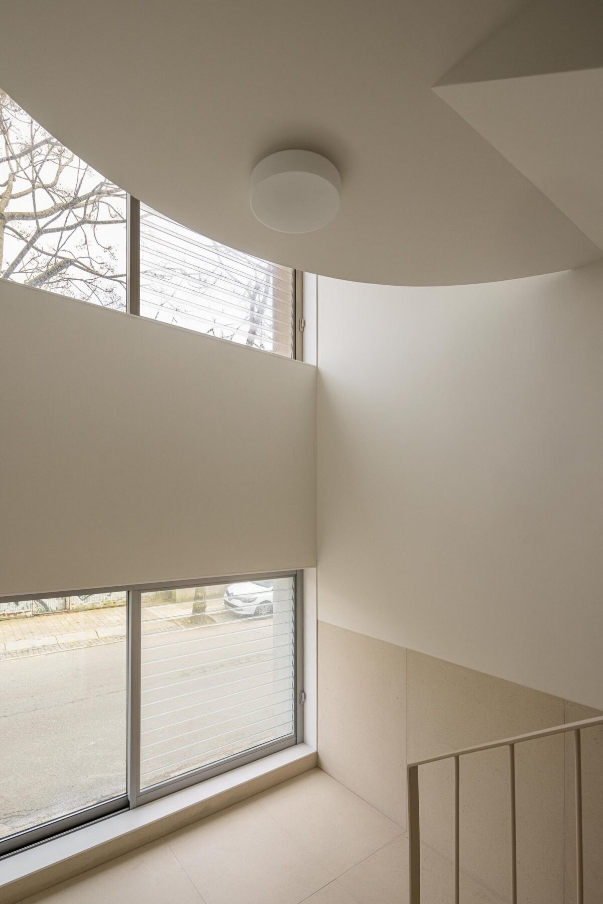 Detalhe da escada com pavimento em pedra clara, guarda metálica e janelas com venezianas, integrando a luz natural no espaço. — EDIFÍCIO DE HABITAÇÃO MULTIFAMILIAR HINTZE RIBEIRO arquitectura HELDER DA ROCHA ARQUITECTOS fotografia Ivo Tavares