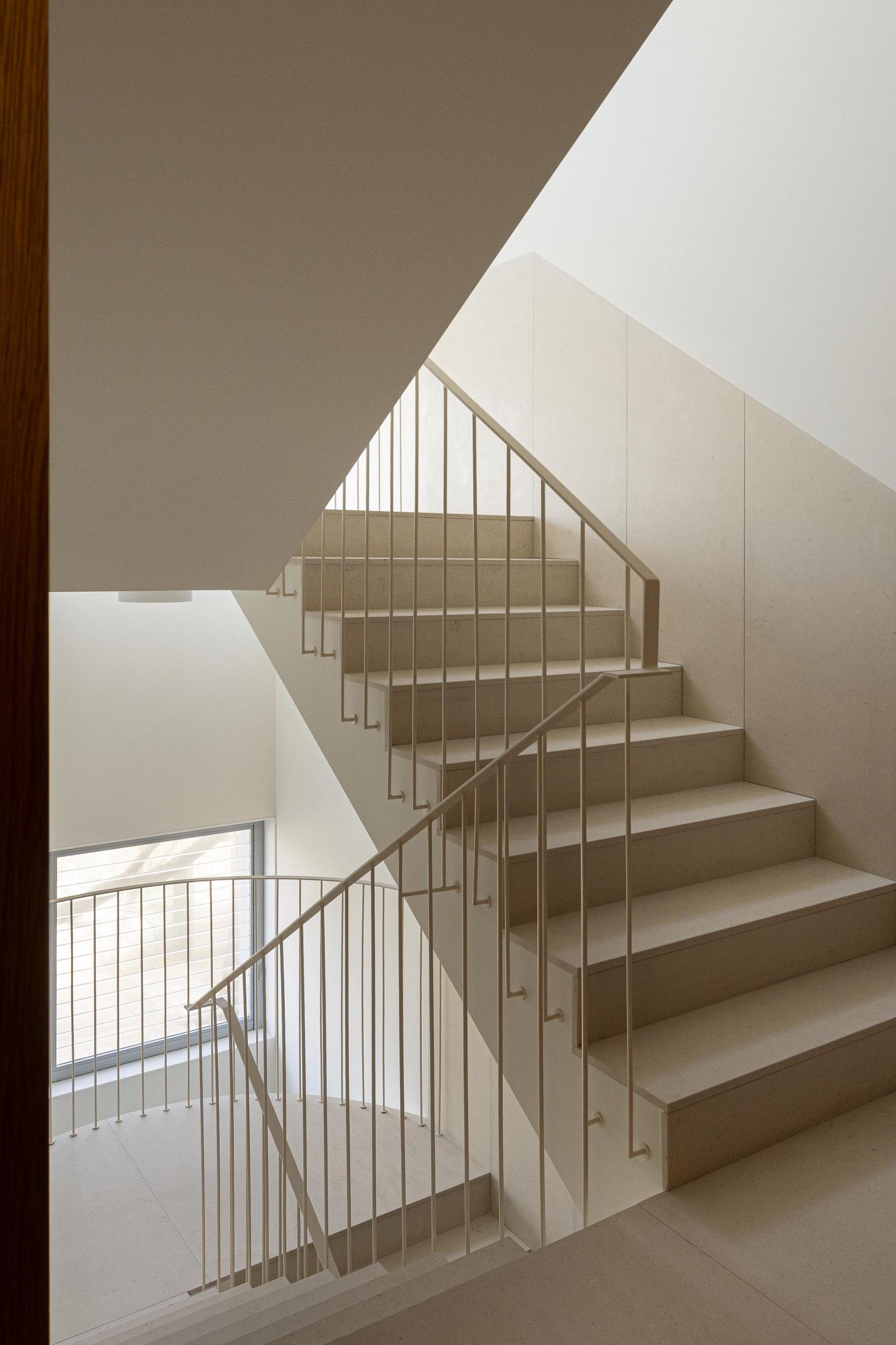 Escadaria interior com degraus e pavimento em pedra calcária clara. Guardas metálicas esguias e paredes brancas recebem luz natural — Edifício Multifamiliar Hintze Ribeiro arquitectura Helder da Rocha fotografia Ivo Tavares