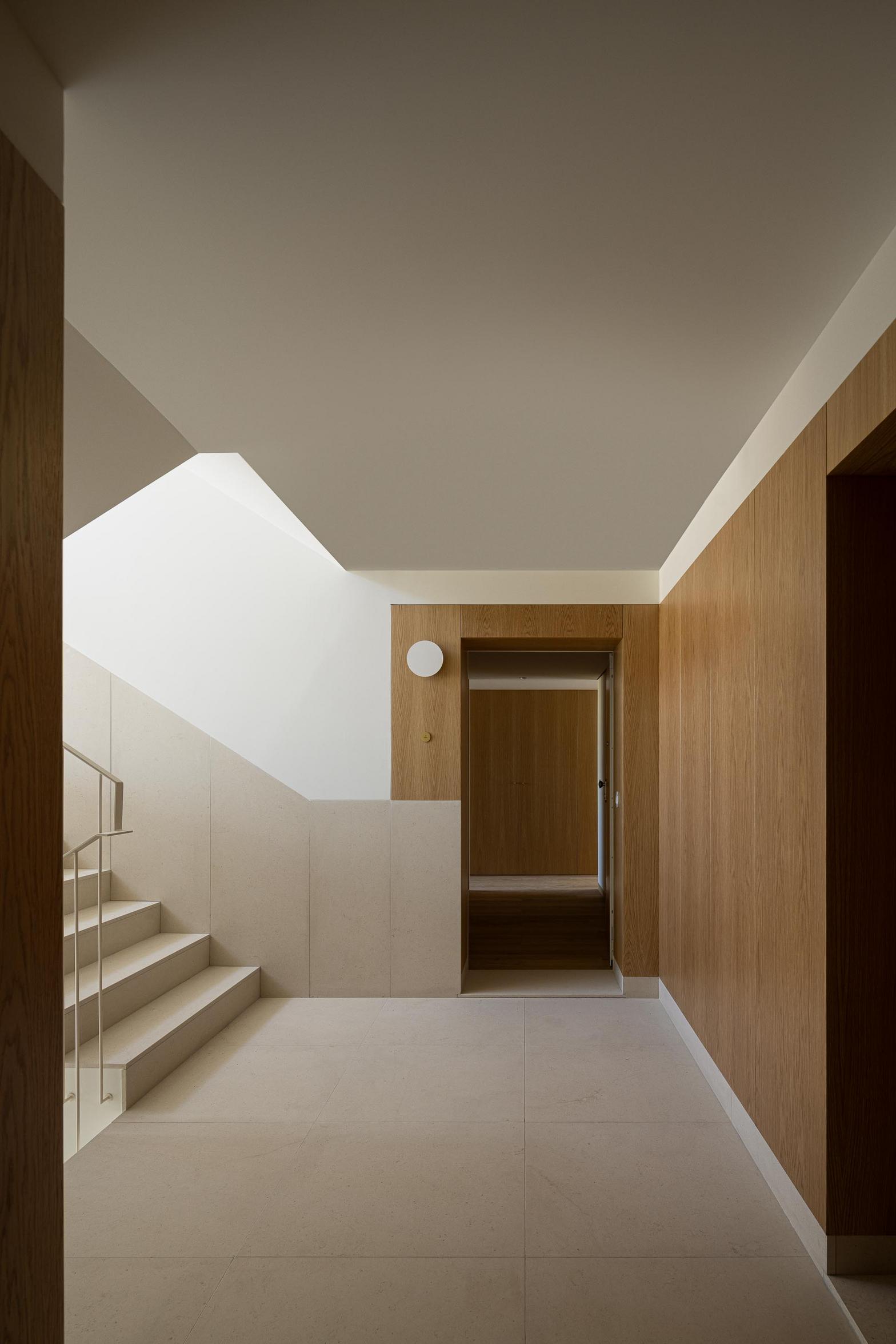 Hall de entrada com pavimento em pedra calcária clara e paredes em madeira de carvalho. Escadaria com guardas metálicas claras — Edifício Multifamiliar Hintze Ribeiro arquitectura Helder da Rocha fotografia Ivo Tavares