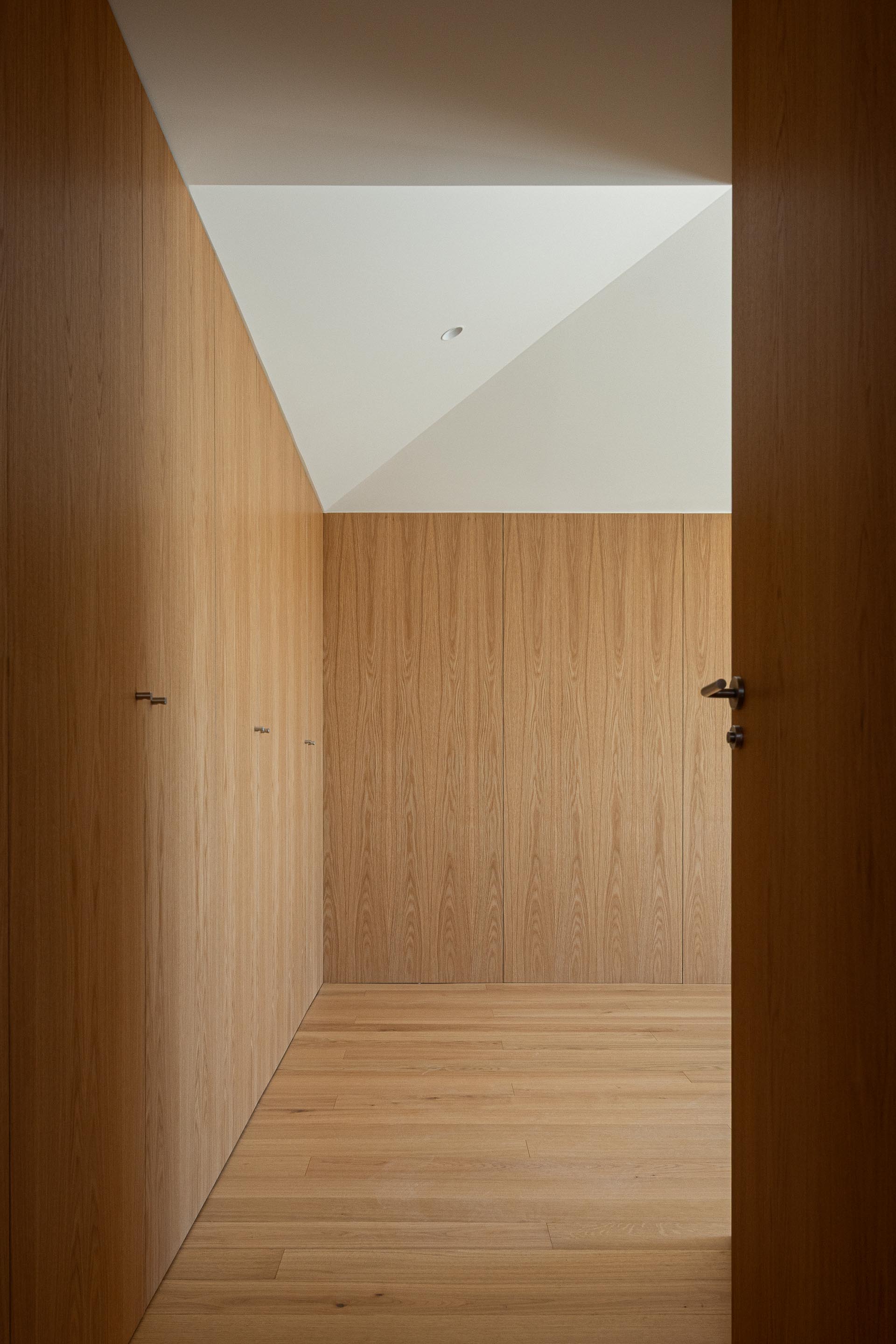 Quarto ou espaço de arrumação com pavimento e paredes em madeira de carvalho. O teto inclinado branco mate recebe luz difusa — Edifício Multifamiliar Hintze Ribeiro arquitectura Helder da Rocha fotografia Ivo Tavares