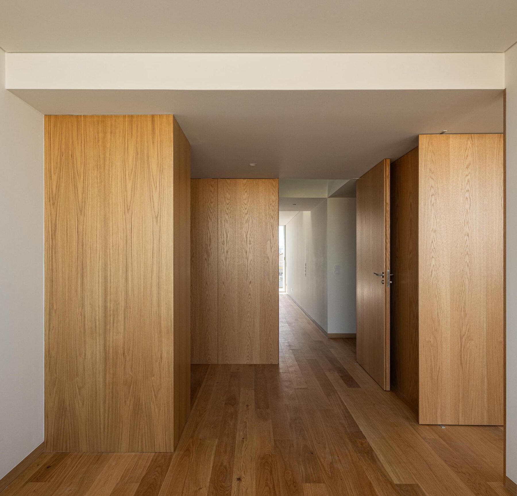 Corredor com revestimento em madeira de carvalho e pavimento em madeira, com portas que definem a circulação e a organização do espaço. — EDIFÍCIO DE HABITAÇÃO MULTIFAMILIAR HINTZE RIBEIRO arquitectura HELDER DA ROCHA ARQUITECTOS fotografia Ivo Tavares