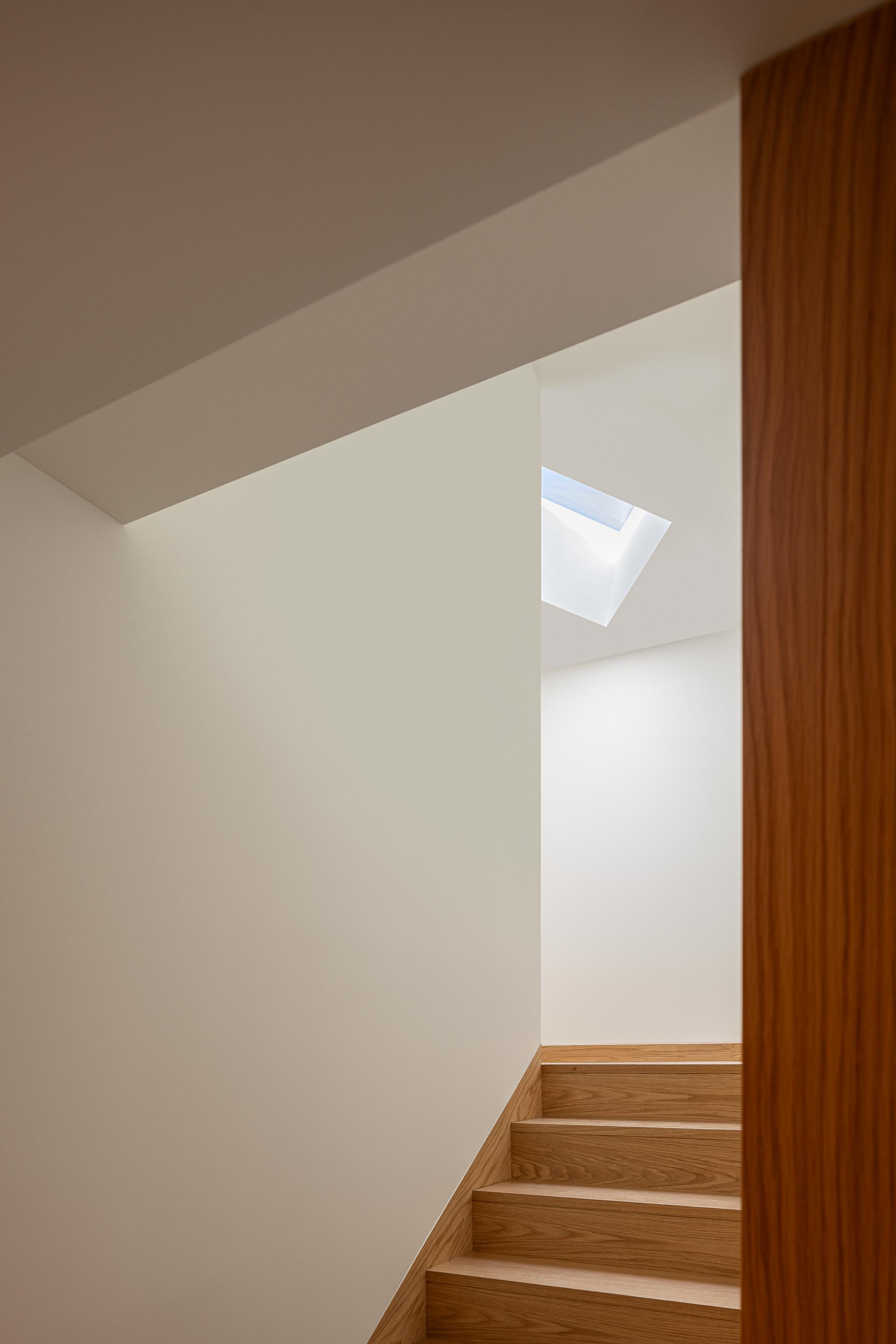 Escadaria com degraus em madeira de carvalho e paredes brancas. Iluminação zenital através de um vão na cobertura, criando um foco de luz — Edifício Multifamiliar Hintze Ribeiro arquitectura Helder da Rocha fotografia Ivo Tavares