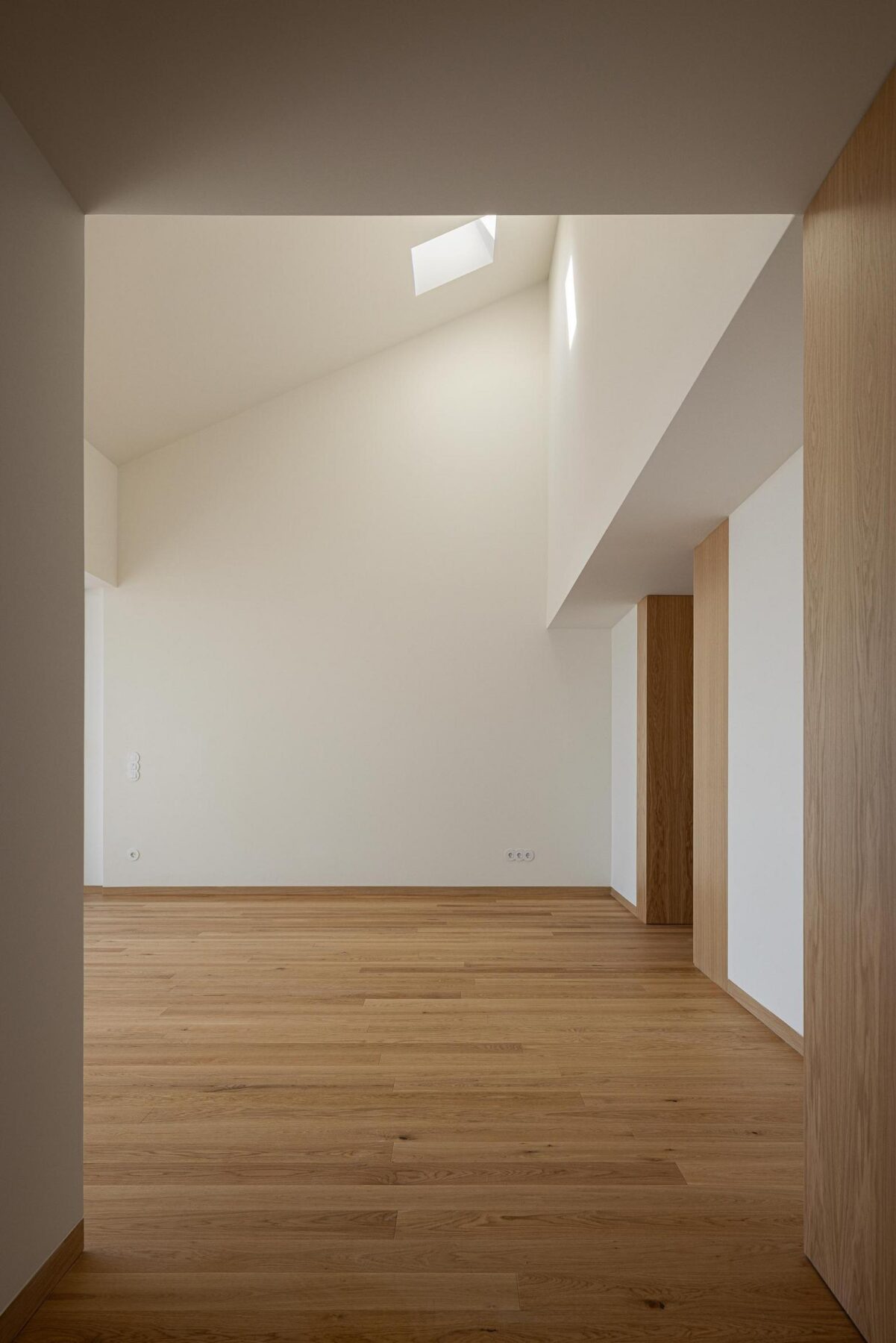 Sala ampla com pavimento em madeira de carvalho, paredes brancas e iluminação zenital, destacando a amplitude e a luminosidade do espaço. — EDIFÍCIO DE HABITAÇÃO MULTIFAMILIAR HINTZE RIBEIRO arquitectura HELDER DA ROCHA ARQUITECTOS fotografia Ivo Tavares