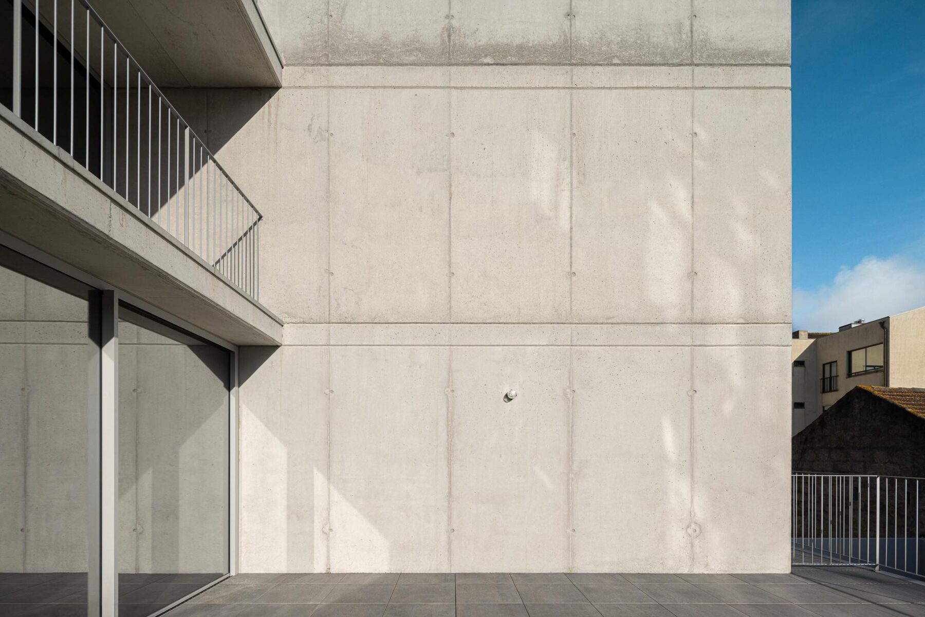 Detalhe da fachada em betão aparente com varanda e vão envidraçado, destacando a textura do material e a luz natural. — EDIFÍCIO DE HABITAÇÃO MULTIFAMILIAR HINTZE RIBEIRO arquitectura HELDER DA ROCHA ARQUITECTOS fotografia Ivo Tavares