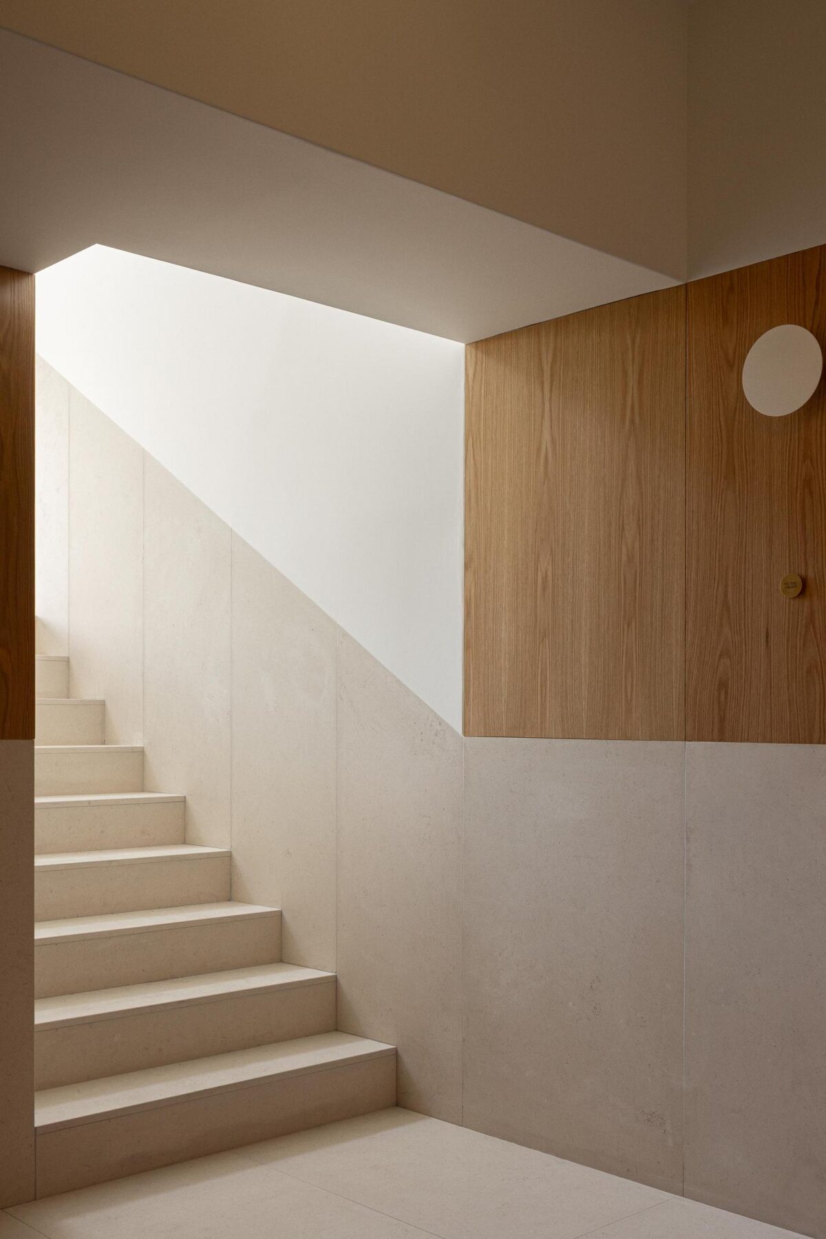 Escada em pedra clara com revestimento em madeira de carvalho, iluminada zenitalmente, criando um ambiente elegante e funcional. — EDIFÍCIO DE HABITAÇÃO MULTIFAMILIAR HINTZE RIBEIRO arquitectura HELDER DA ROCHA ARQUITECTOS fotografia Ivo Tavares
