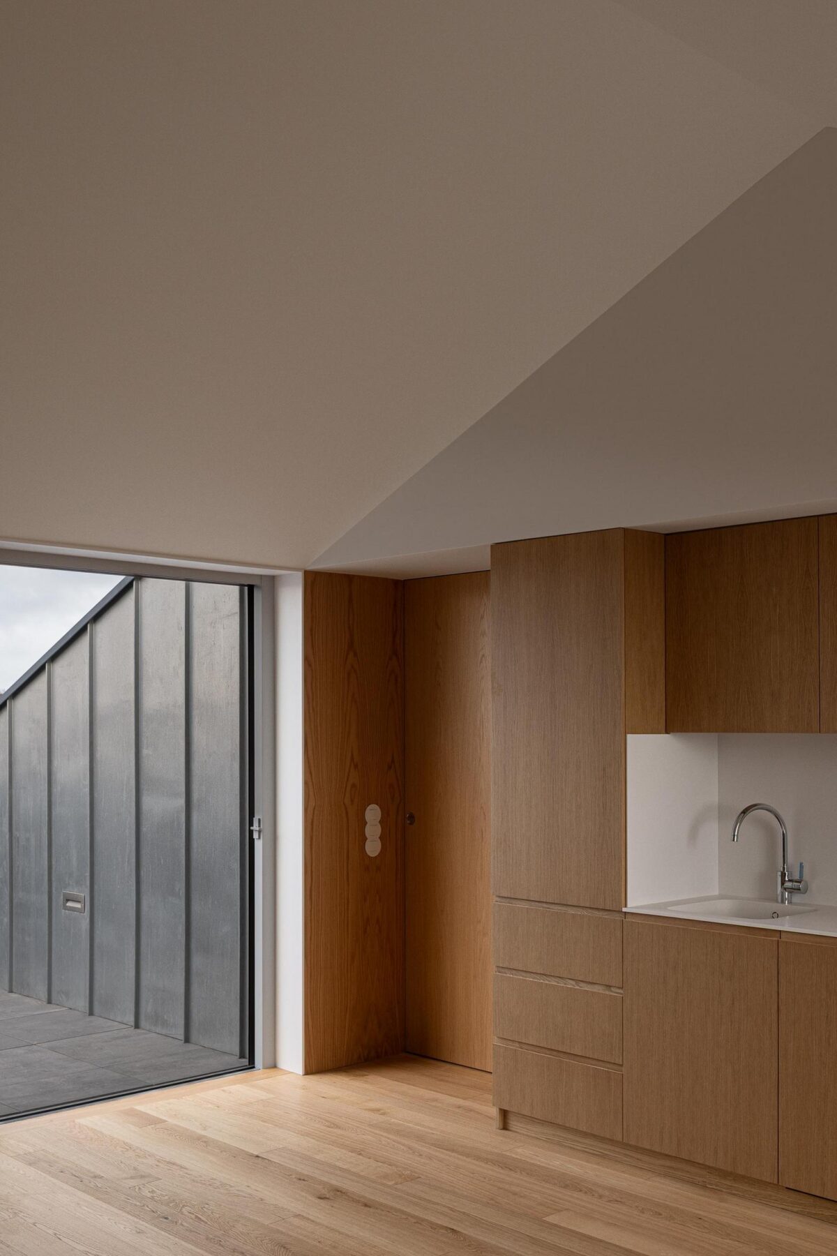 Cozinha com armários em madeira de carvalho e acesso ao terraço com revestimento metálico, integrando os espaços interior e exterior. — EDIFÍCIO DE HABITAÇÃO MULTIFAMILIAR HINTZE RIBEIRO arquitectura HELDER DA ROCHA ARQUITECTOS fotografia Ivo Tavares