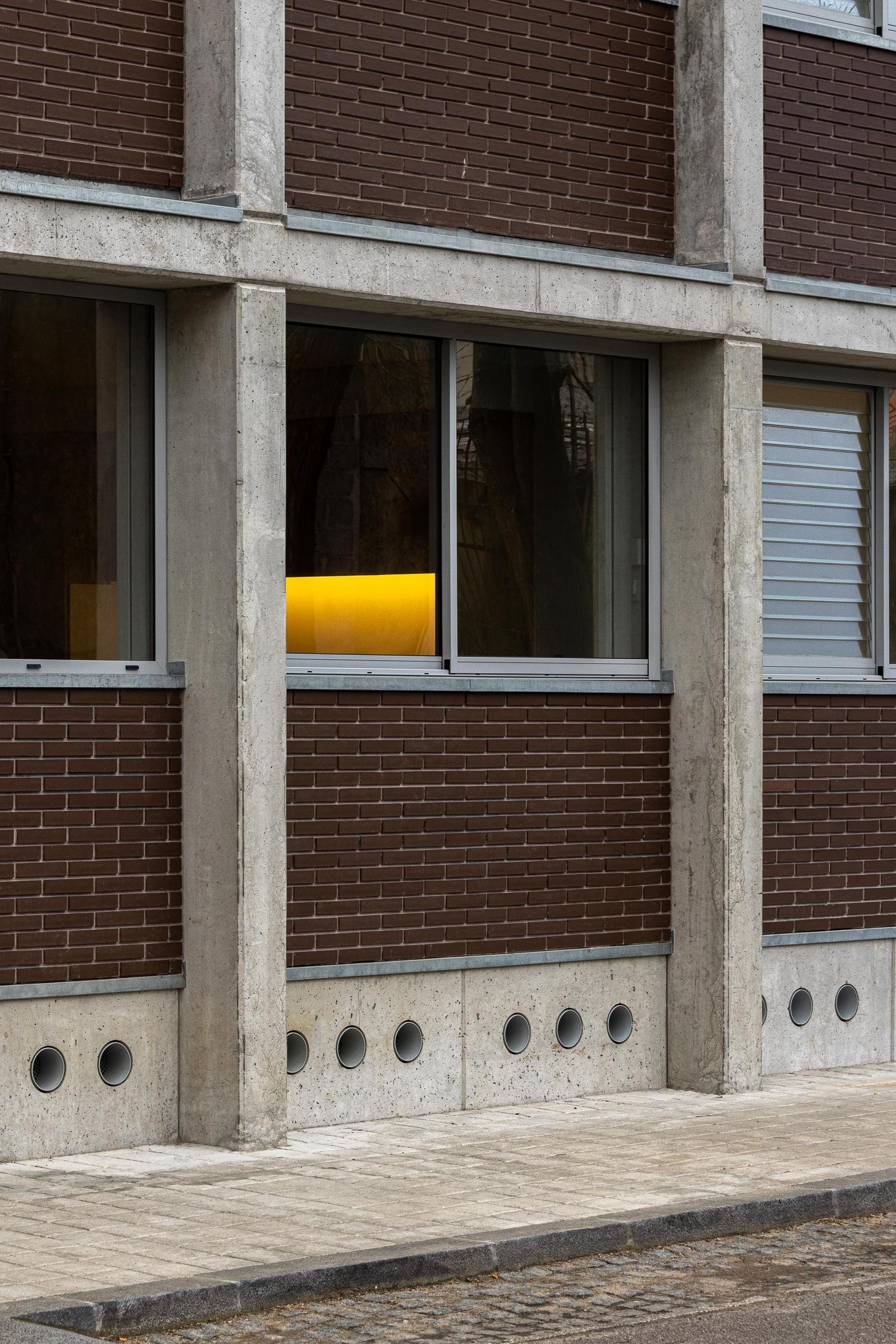 Detalhe da fachada de betão aparente cinzento e tijolo maciço castanho. Vãos com caixilharia metálica e grelhas de ventilação circulares — Edifício Multifamiliar Hintze Ribeiro arquitectura Helder da Rocha fotografia Ivo Tavares