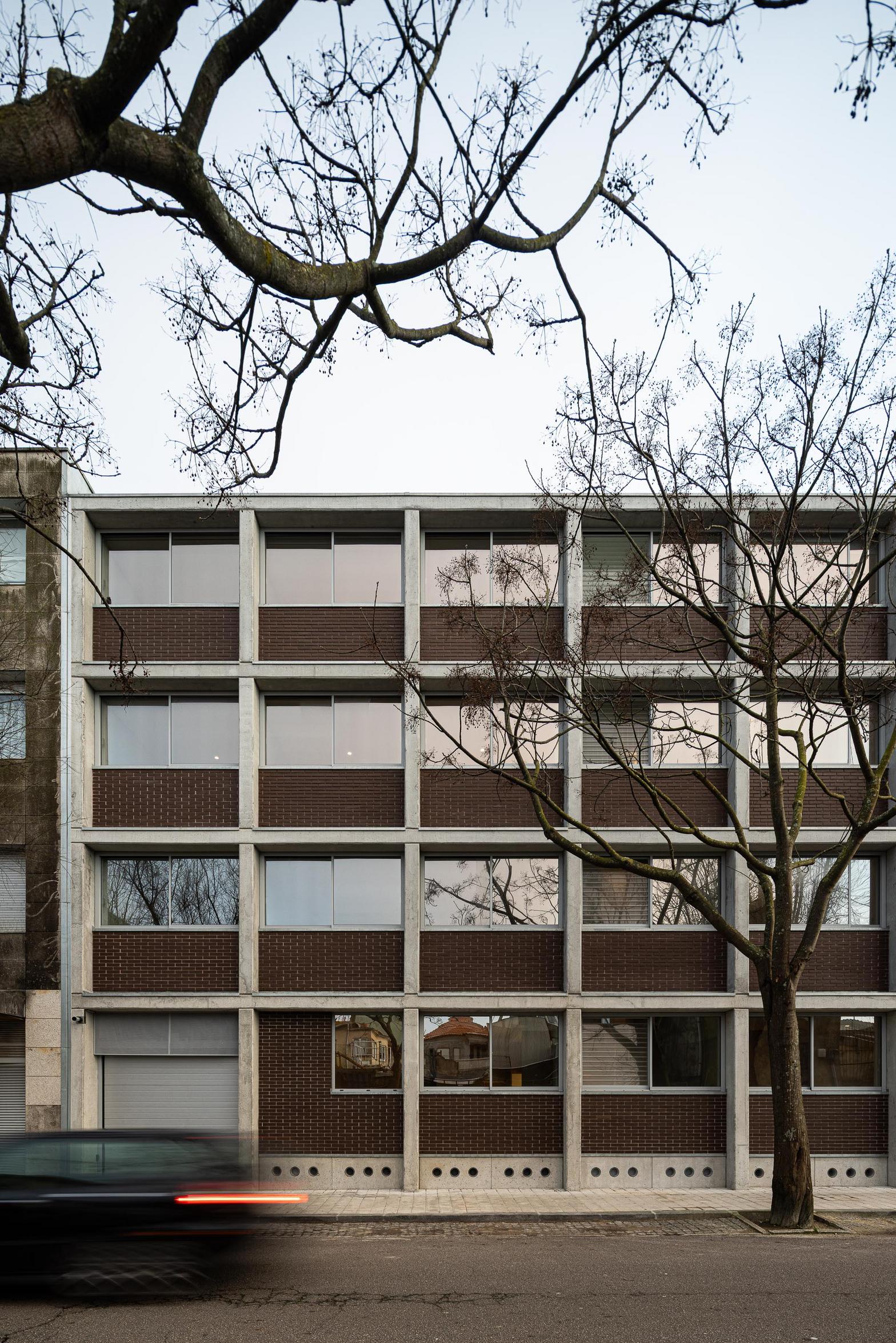 Fachada de betão aparente cinzento e tijolo maciço, com vãos ritmados. A estrutura em betão moldado in situ define a volumetria — Edifício Multifamiliar Hintze Ribeiro arquitectura Helder da Rocha fotografia Ivo Tavares