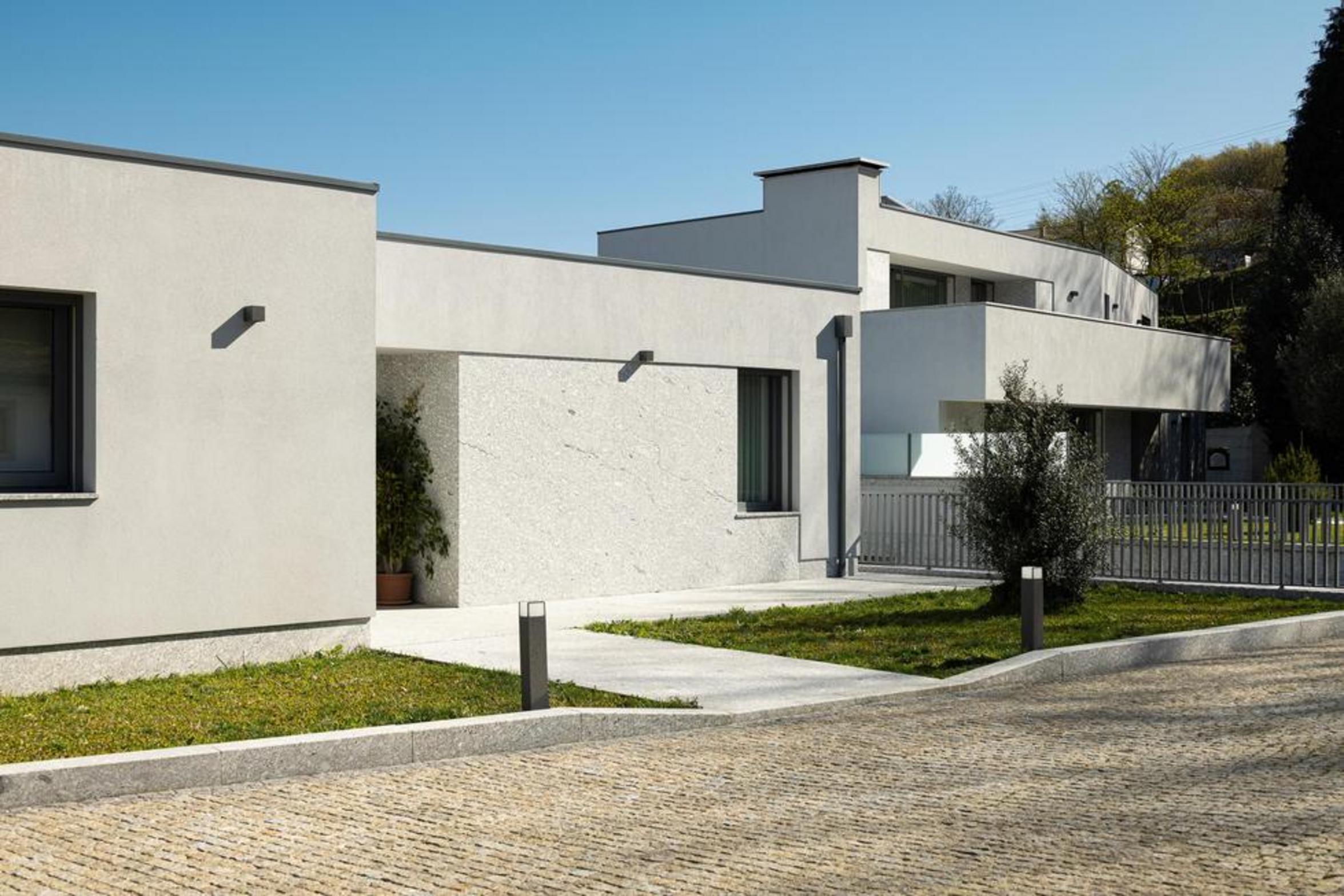 Fachada frontal das moradias. Volumes brancos e embasamento em pedra clara. Caminhos em betão e relva, integrando-se no lote — Duas Casas em Guimarães arquitectura Félix Arquitectos fotografia Ivo Tavares