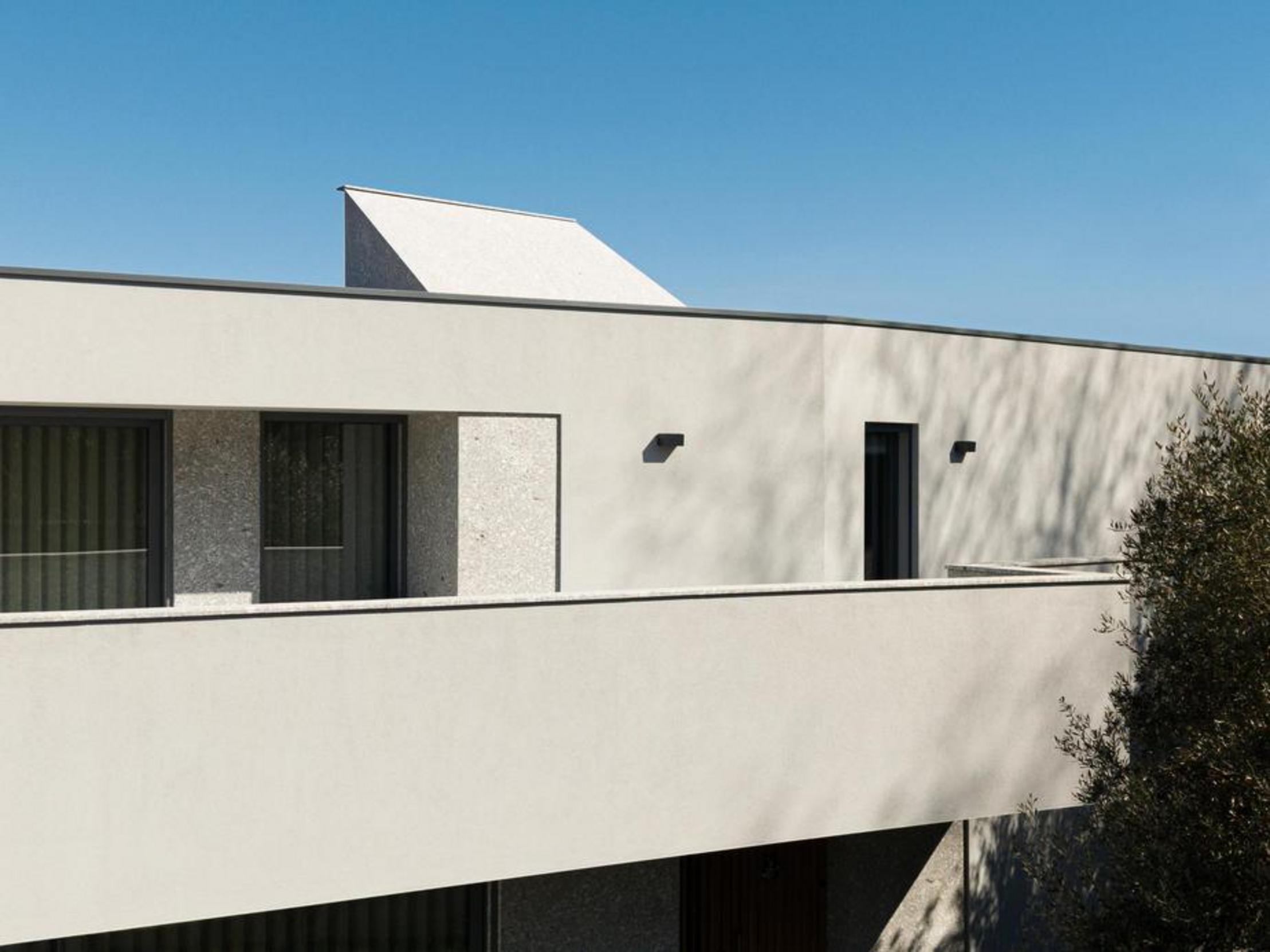 Fachada superior com revestimento branco e apontamentos em pedra clara. Vãos retangulares e elemento escultórico na cobertura plana — Duas Casas em Guimarães arquitectura Félix Arquitectos fotografia Ivo Tavares