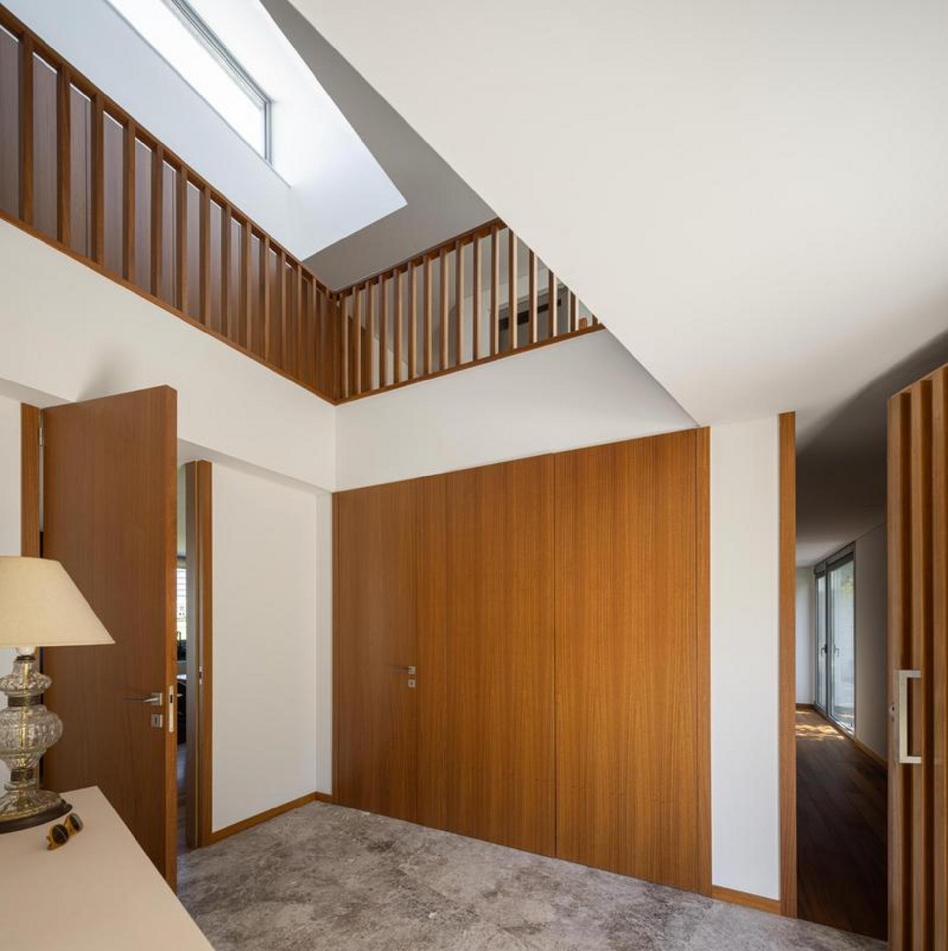 Hall de entrada com pé-direito duplo. Pavimento em pedra, paredes brancas e painéis de madeira. Guarda-corpos de madeira no piso superior — Duas Casas em Guimarães arquitectura Félix Arquitectos fotografia Ivo Tavares