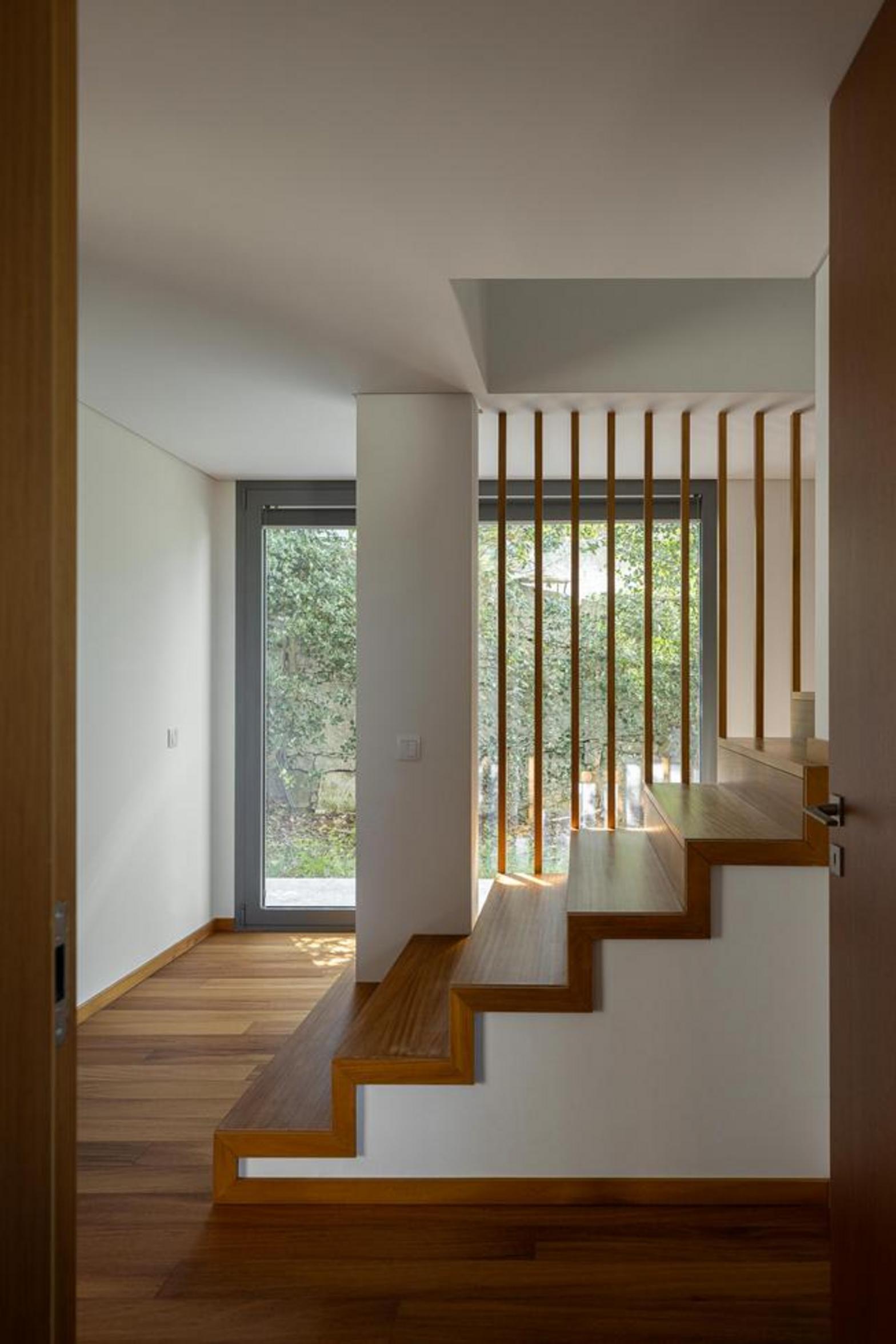 Escada interior com degraus e guarda-corpos em madeira. Paredes brancas e vão envidraçado com vista para a vegetação exterior — Duas Casas em Guimarães arquitectura Félix Arquitectos fotografia Ivo Tavares